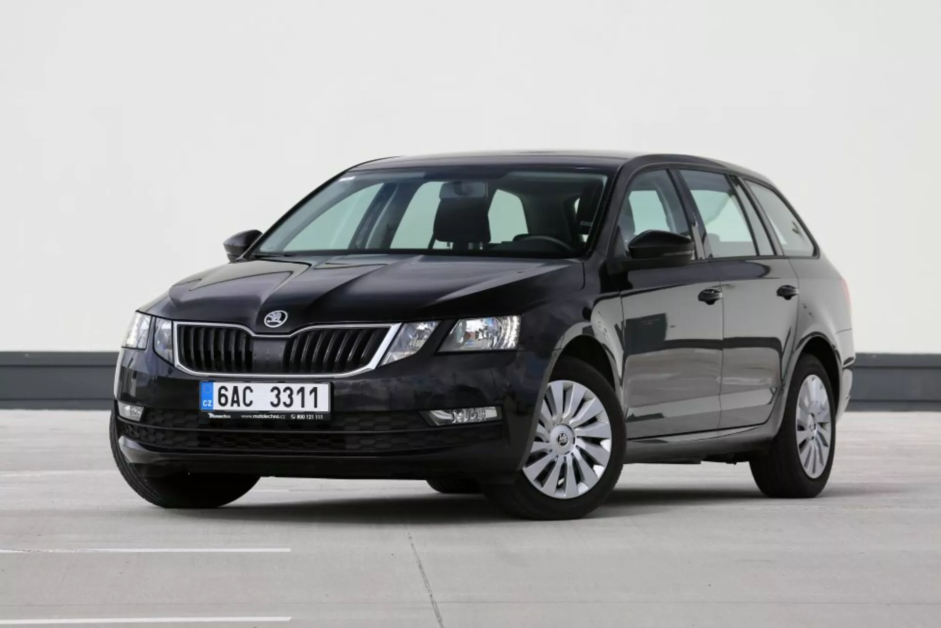 Mozdulatlan Škoda jármű, amelyet a vezető oldali háromnegyedes elülső perspektívából látni, bemutatva a rácsot, a fényszórókat, a motorháztetőt, a szélvédőt, az első vezető és a hátsó utas ajtóit, a tető egy részét és a bal oldali tükröt egy sík belső felületen profi világítással