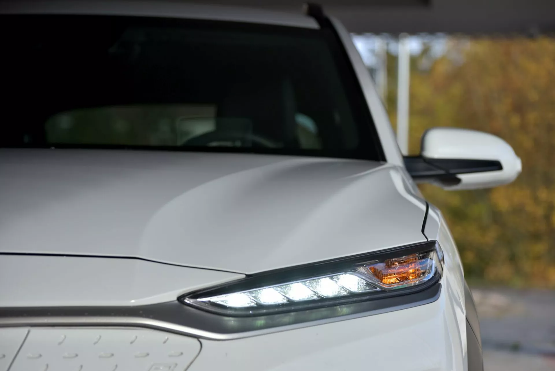 2021-es Hyundai Kona Elektro közelkép a bal első résszel, LED fényszóróval, nappali menetfényekkel és esőcseppekkel a fémes karosszérián