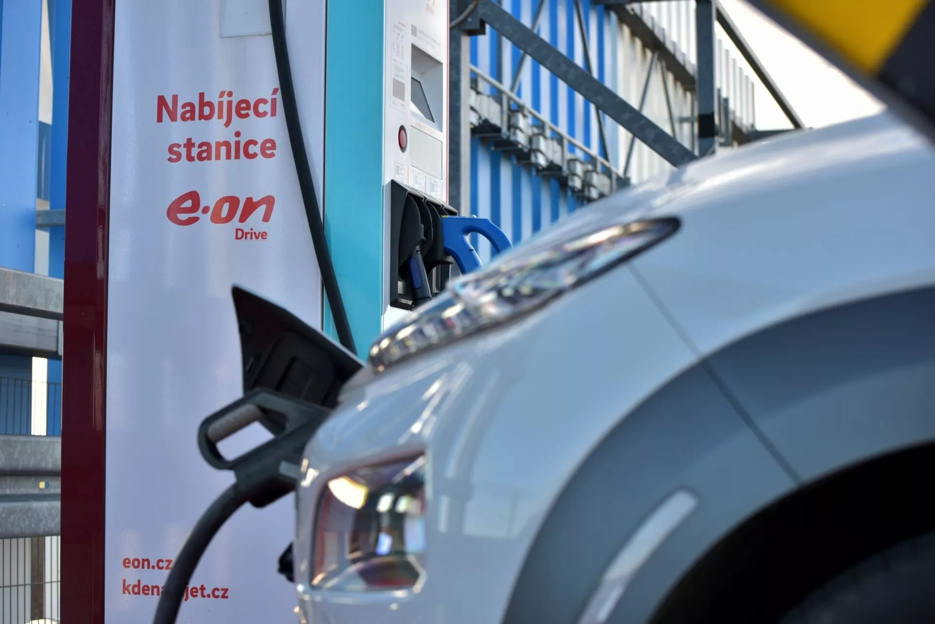 2021-es Hyundai Kona Electric töltés közben egy E.ON Drive állomáson, bemutatva a jármű bal első negyedét, nyitott töltőportot a csatlakoztatott kábellel, és a modern LED fényszóró tervezését