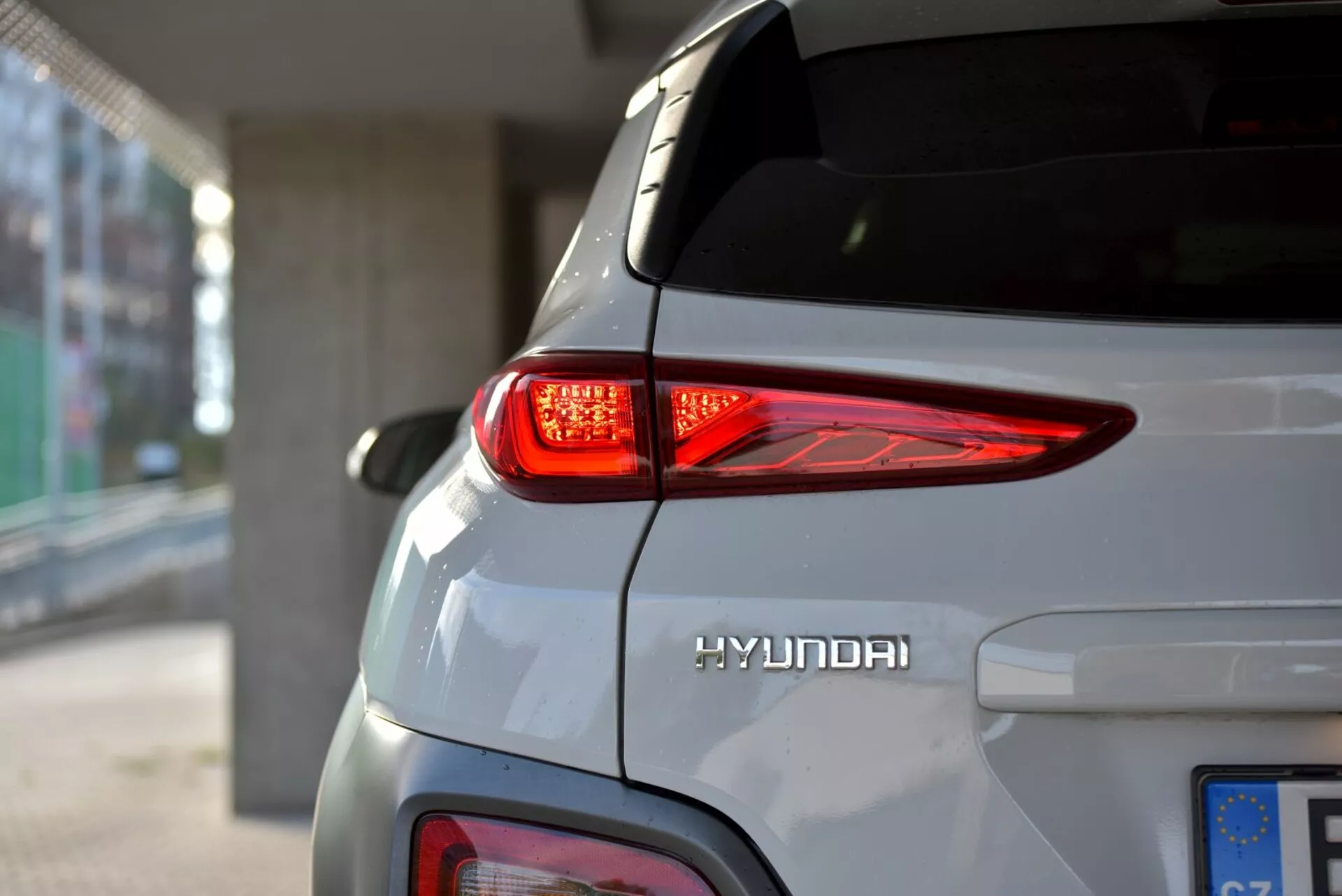 Közeli nézet a 2021-es Hyundai Kona Electric hátsó jobb oldalára, kiemelve a görbe LED hátsó lámpát, a Hyundai logót és az elegáns ezüst karosszériát természetes fényben