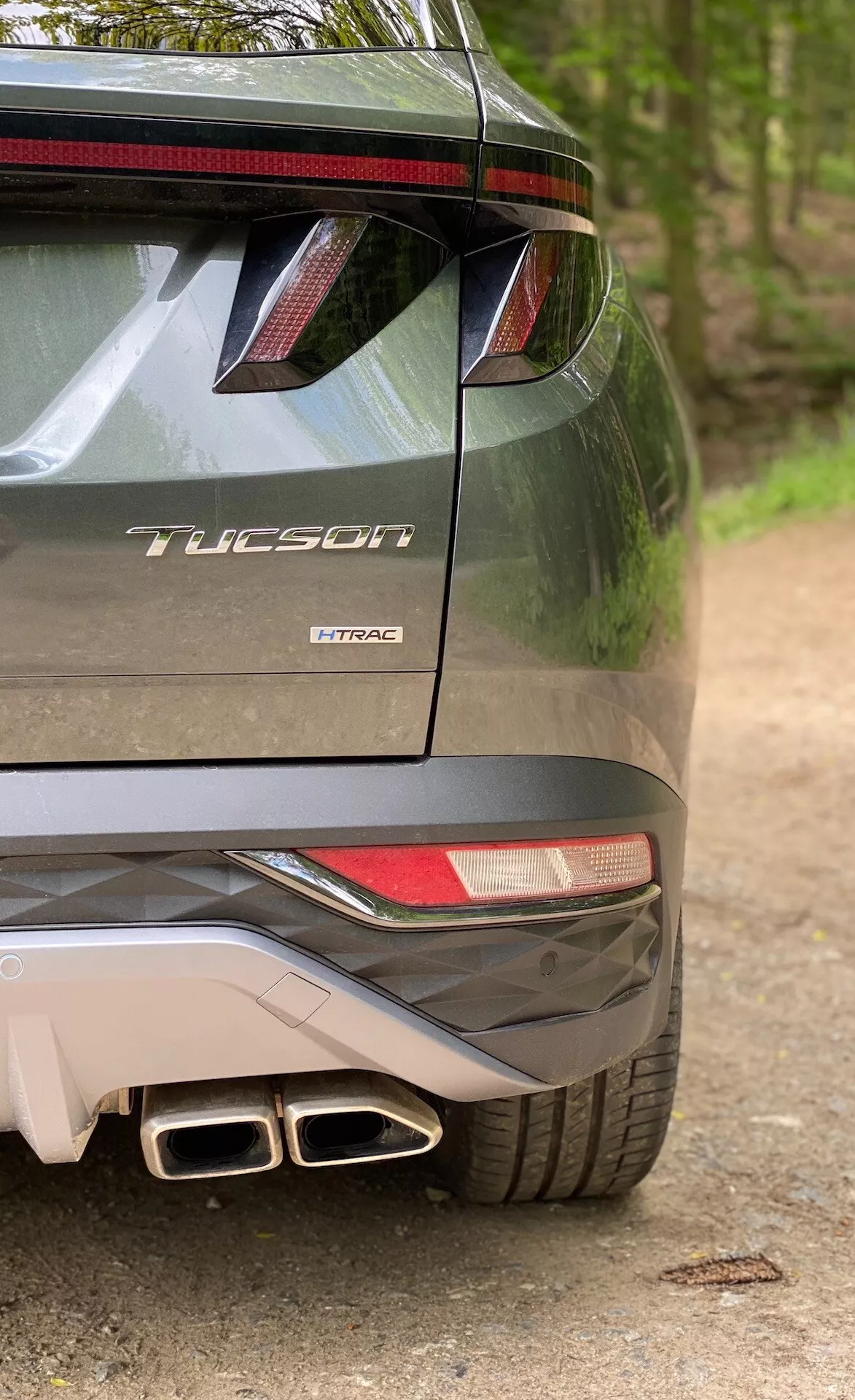 A 2020-as Hyundai Tucson modell részleges hátsó nézete, amely azt jelzi, hogy ez az 1.6 T-GDi Pure változat, megmutatva a lökhárító jobb oldalát, a részleges hátsó lámpát, a LED-es féklámpával felszerelt hátsó spoilert, a dupla kipufogóvégeket és a modellszámot a 'Tucson' névvel és a 'T-GDi' motortechnológiával.