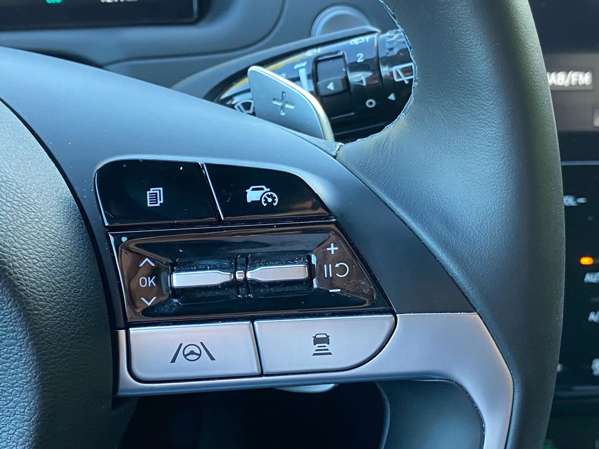 Közelkép a 2020-as Hyundai Tucson 1.6 T-GDI Pure kormánykerék baloldali kezelőszerveiről, amelyek olyan funkciókat mutatnak be, mint a menünavigáció, az audiohangerő szabályozása, a hangvezérlés aktiválása és a Bluetooth telefonhívás funkció.