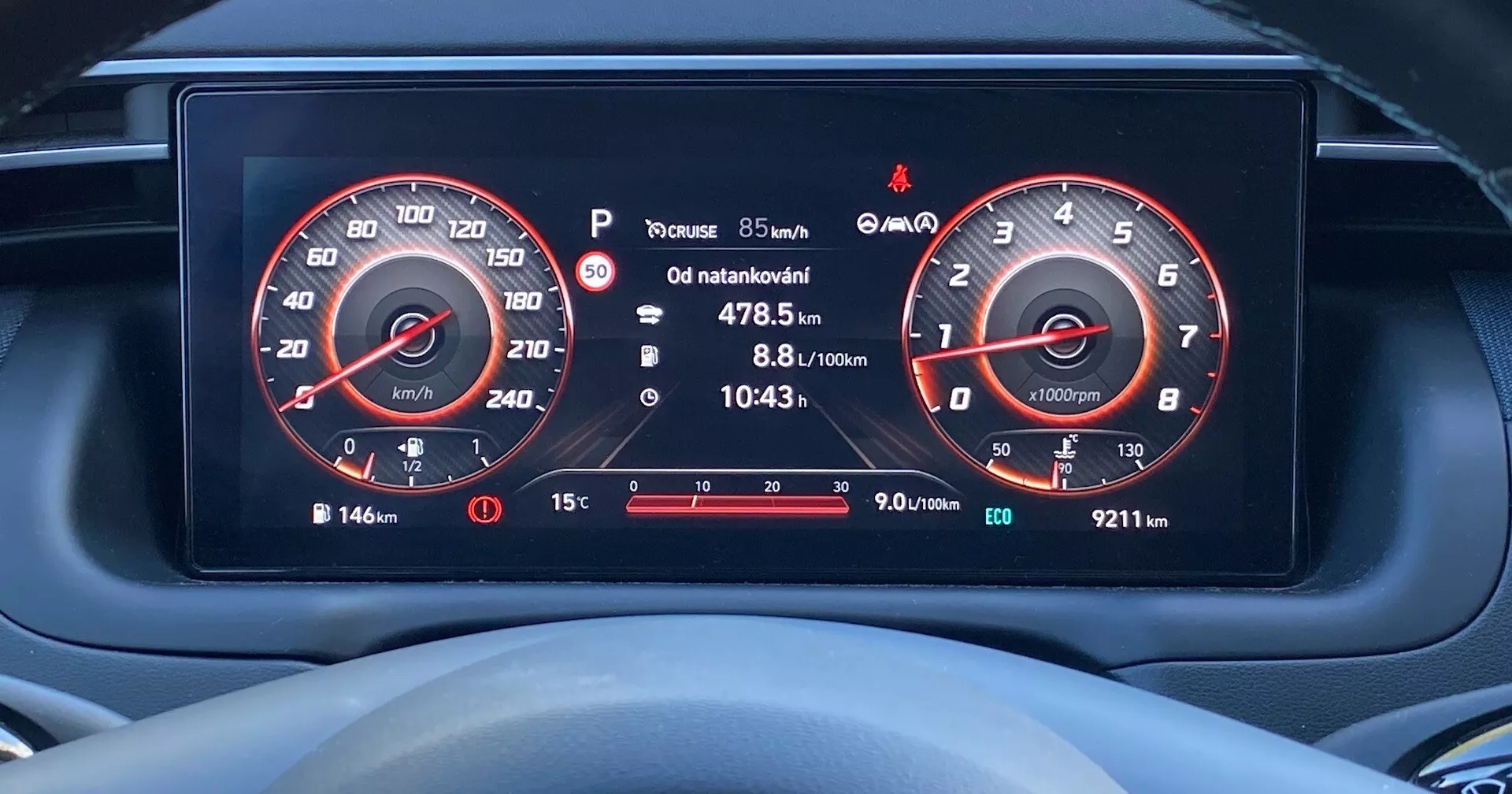 Közelkép egy Hyundai Tucson 2020 digitális műszerfaláról a vezető szemszögéből, amely nagy felbontású kijelzőket mutat a sebességmérőről (260 km/h-ig) és a fordulatszámmérőről (7000 rpm-ig), üzemanyagszintmérőt, utazási információkat, gumiabroncs nyomás figyelmeztetést, külső hőmérsékletet és különböző figyelmeztető ikonokat.