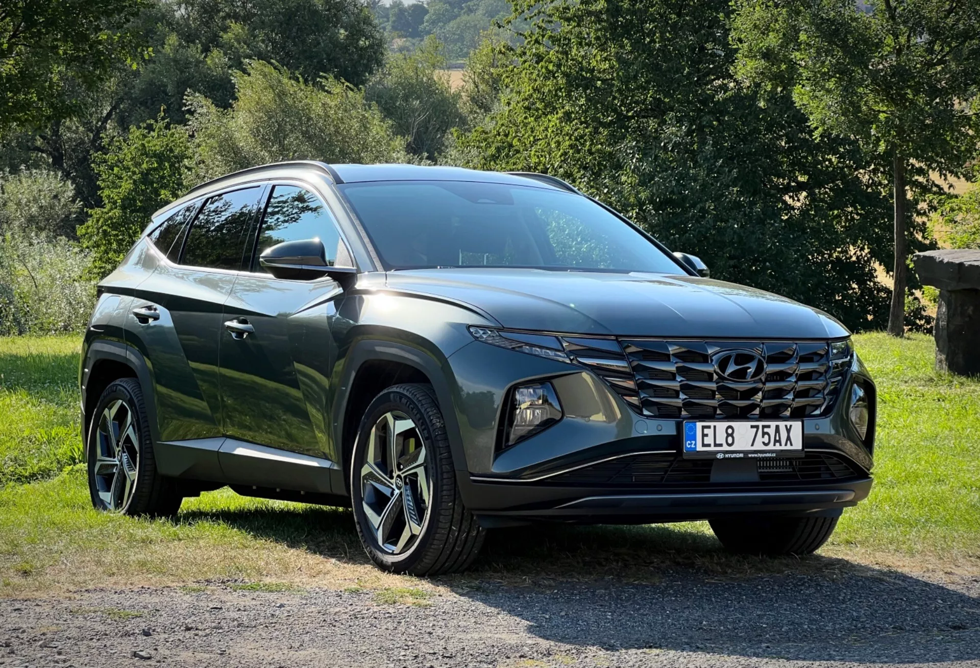 2020-as Hyundai Tucson a fűön parkolva vidéki háttérrel, megmutatva a háromnegyedes első perspektívát a részletes nézet érdekében a karcsú LED fényszóróiról, szögletes első hűtőrácsáról és fényes sötét színű bevonatáról