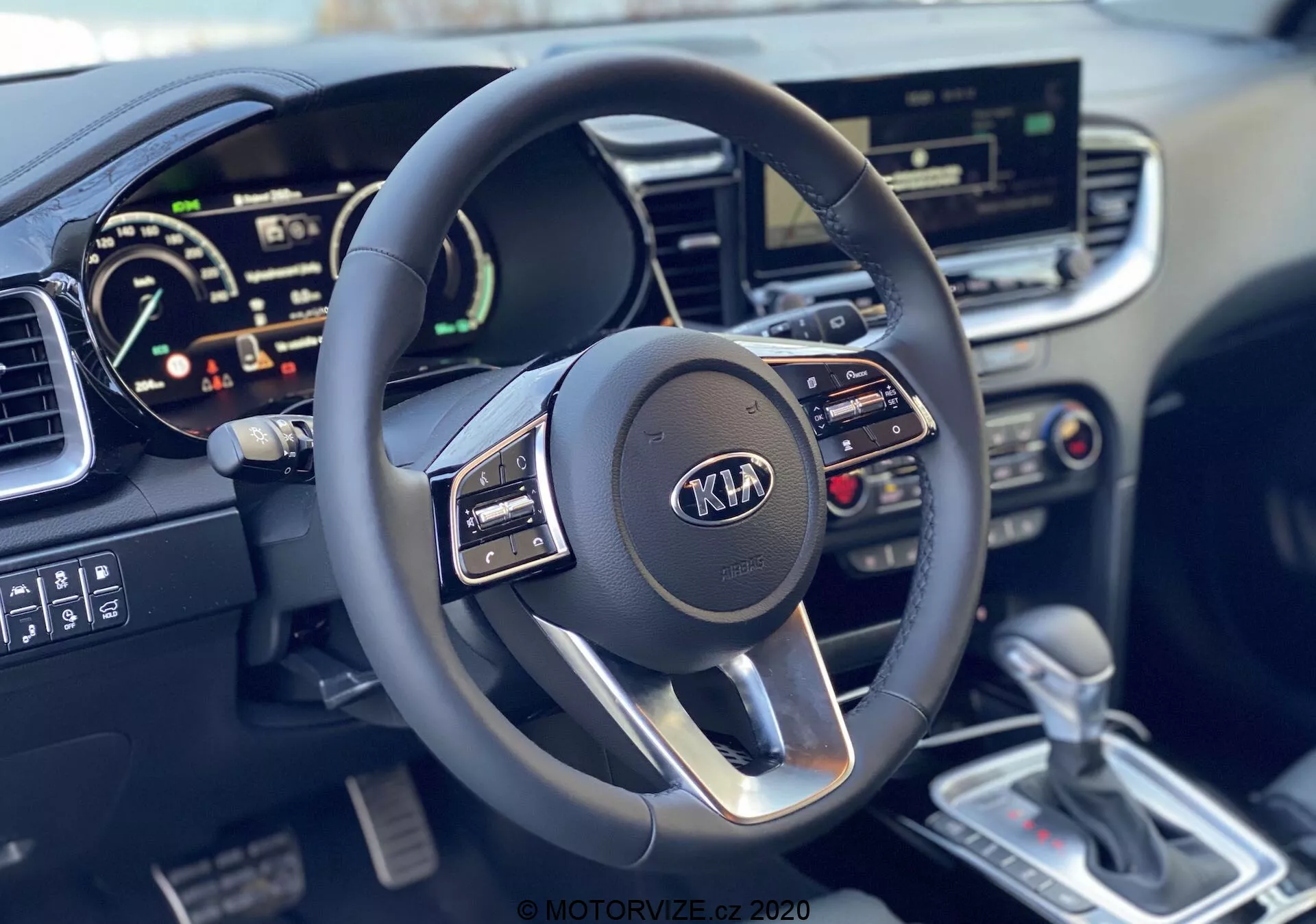 Első személyű nézet a 2018-as Kia Ceed belső teréről, kiemelve a modern háromküllős multifunkcionális kormánykereket Kia logóval és a digitális műszercsoportot, amely a sebességmérőt és a lehetséges fordulatszámmérőt mutatja, valamint az érintőképernyős infotainment rendszert, a klímavezérlőket, az ezüstszínű automatikus sebességváltót és a részletes középkonzolt.