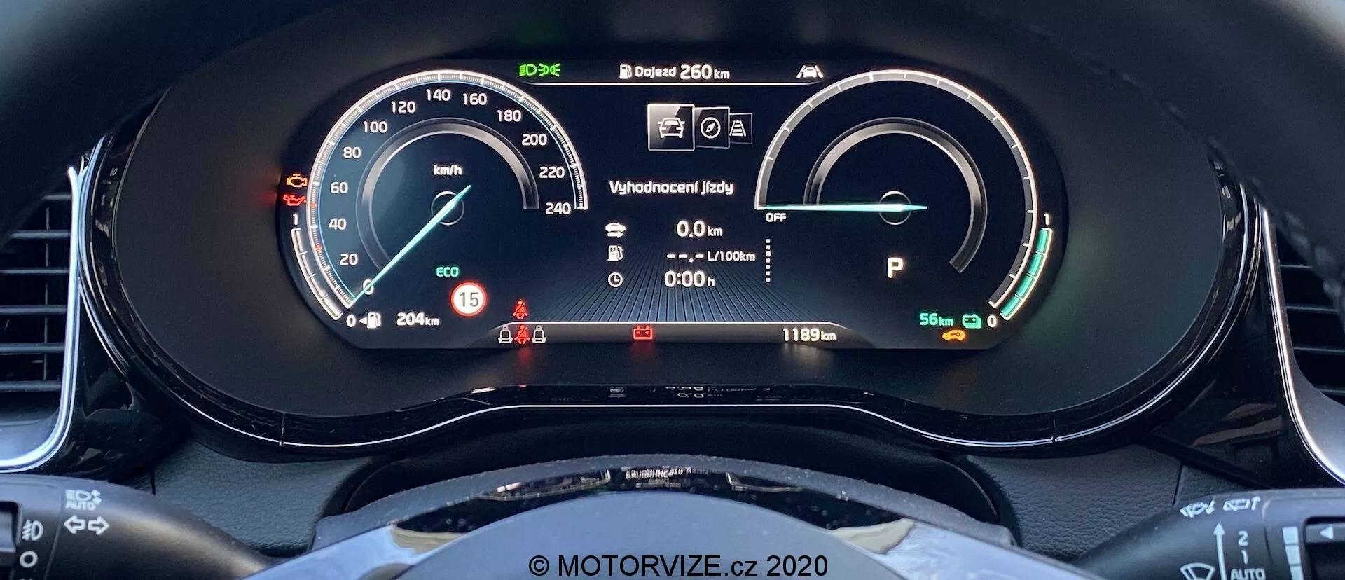 Közelkép a 2018-as Kia Ceed digitális műszerfaláról a vezetőülés perspektívájából. A kijelző tartalmaz egy analóg mutatós és digitális leolvasású sebességmérőt, amely 15 km/h-t mutat. A jobb oldalon egy teljesen feltöltött akkumulátorral és 481 km-es hatótávval rendelkező teljesítmény/akku mérő található. Egyéb elemek között szerepel a kész állapot kijelzése, a vezetői információ megjelenítése figyelmeztető lámpákkal, 20,5°C-os külső hőmérséklet-olvasó és a Park módban lévő jármű. Látható a sportos, lapos aljú kormánykerék felső íve is.