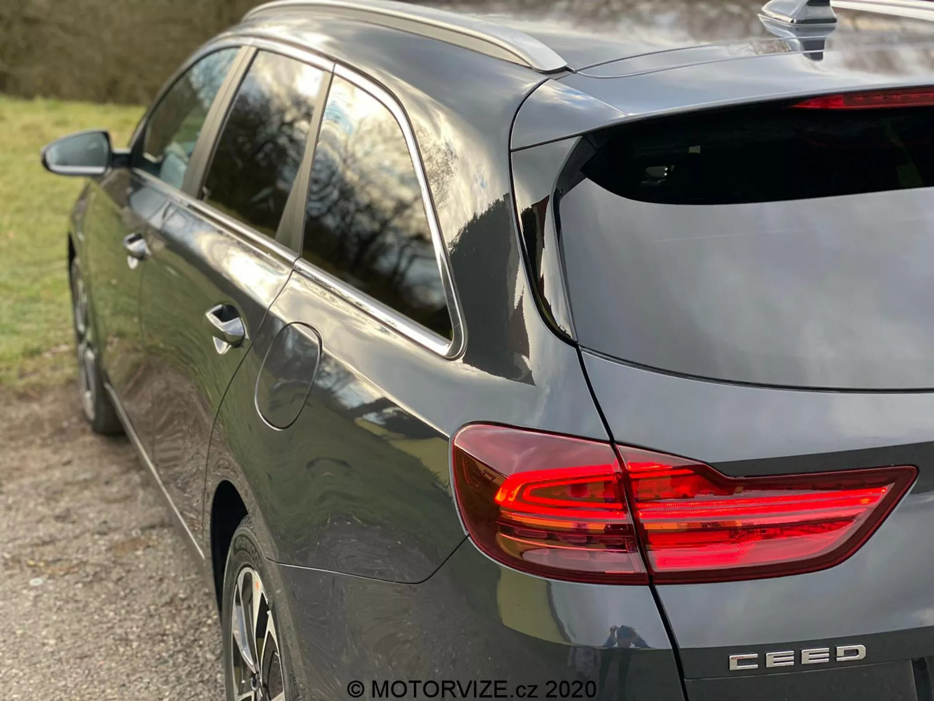 Részleges oldalsó és hátsó nézet egy modern, szürke színű Kia Ceed 2018-as ferdehátú autóról, kiemelve a világító C alakú LED hátsó lámpát, hátulján ablaktörlővel és diszkrét tető-spoilerrel rendelkező ferdehátú dizájnt, cápauszony antennát, alufelniket és márkajelzést a 'CEED' modellnévvel, amely természetes késő délutáni napfényben és kis élességű mélységgel készült, a járműre összpontosítva.