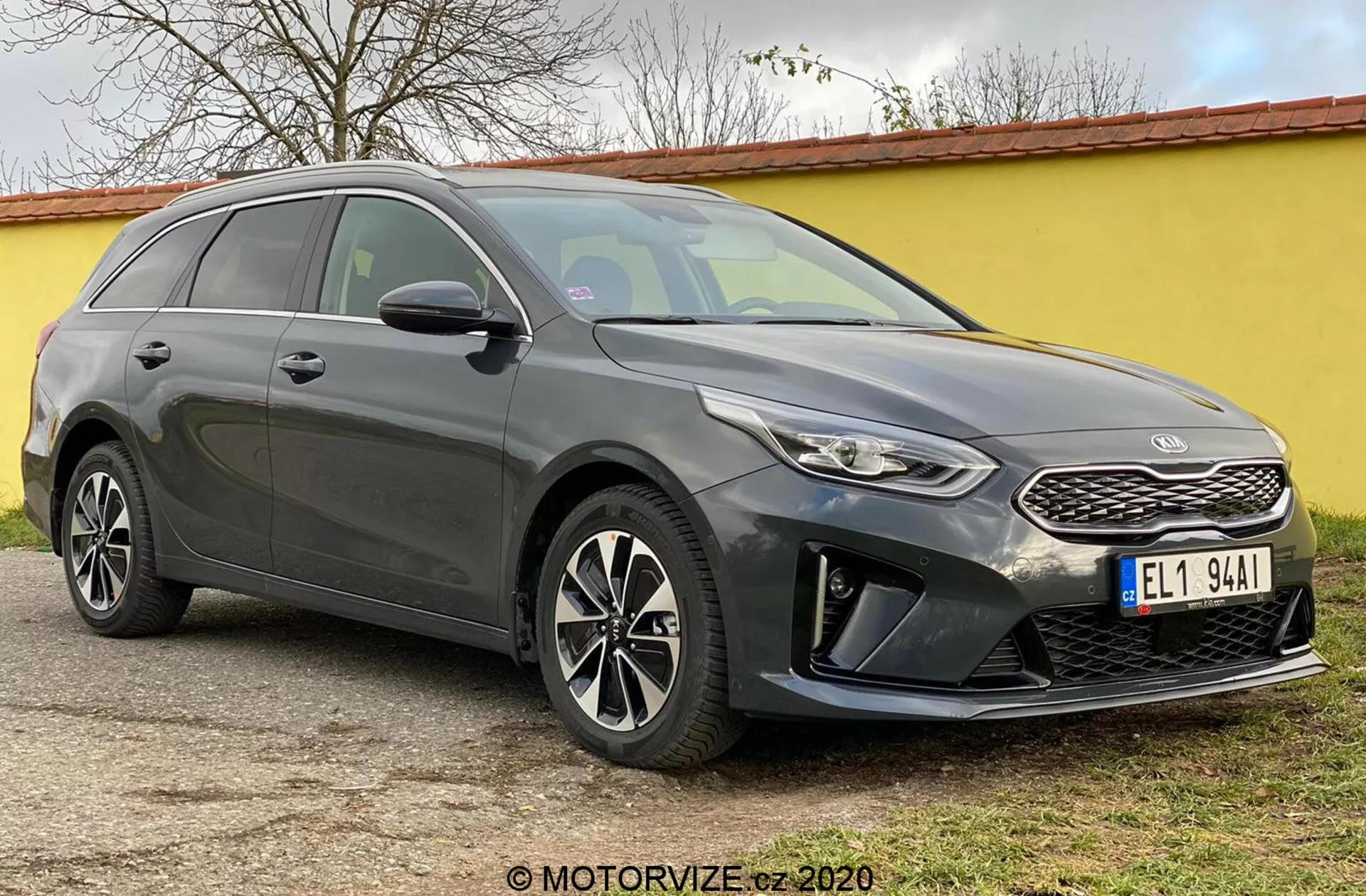 A képen a 2018-as Kia Ceed látható, egy modern kombi, amelyet elölről háromnegyedes szögből fényképeztek, kiemelve első részét, beleértve a strukturált hűtőrácsot egy jellegzetes márka emblémával, keskeny visszahúzódó fényszórókat LED nappali menetfénnyel és egy első lökhárítót ködlámpa házakkal és parkolóérzékelőkkel. A motorháztető elegáns kontúrvonalai a meredeken dőlt szélvédőhöz vezetnek, ezáltal hangsúlyozva az autó aerodinamikai profilját. Láthatók a többküllős alufelnik és az integrált irányjelzős oldalsó tükrök, valamint a lefelé ívelő tetővonal a hátul felé és a tetősínek, amelyek mind a stílust, mind a hasznosságot kiemelik. Az árnyékolt ablakok és a karosszéria vonalai az oldal mentén szoborszerű megjelenést kölcsönöznek. Az autó egy sík külső felületen áll.