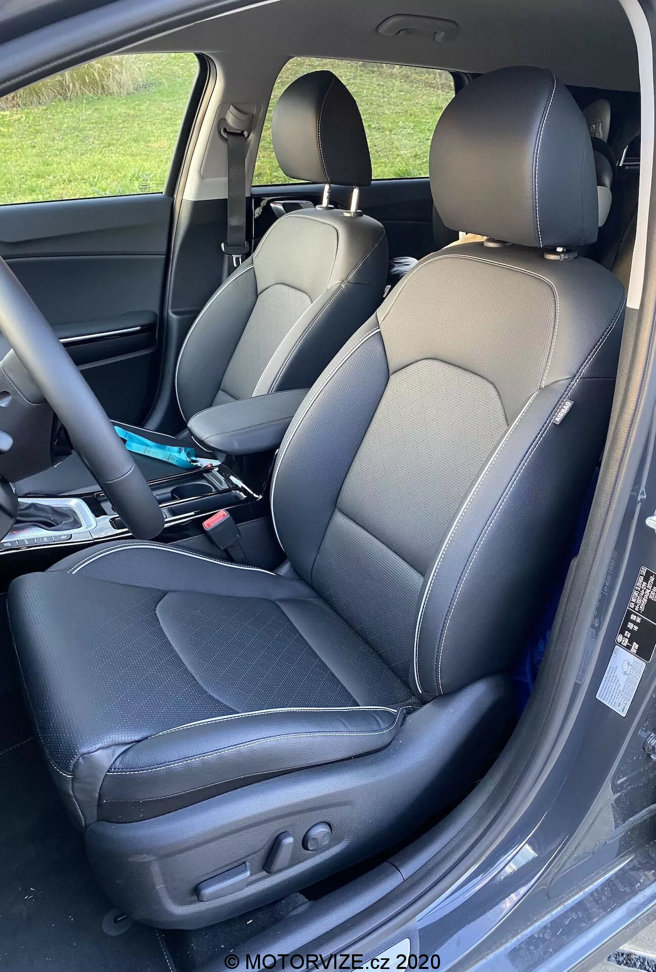 A 2018-as Kia Ceed belső terének közeli részlete, amely a vezető és az utasüléseket mutatja két tónusú bőr kárpitozással, kontrasztos varrással, oldaltámaszos sportülés kialakítással és elektromos beállításokkal a vezetőülés háttámlájának és pozíciójának szabályozásához. Enyhe gyűrődések használatra utalnak, és különféle tárgyak láthatók az utasülésen.