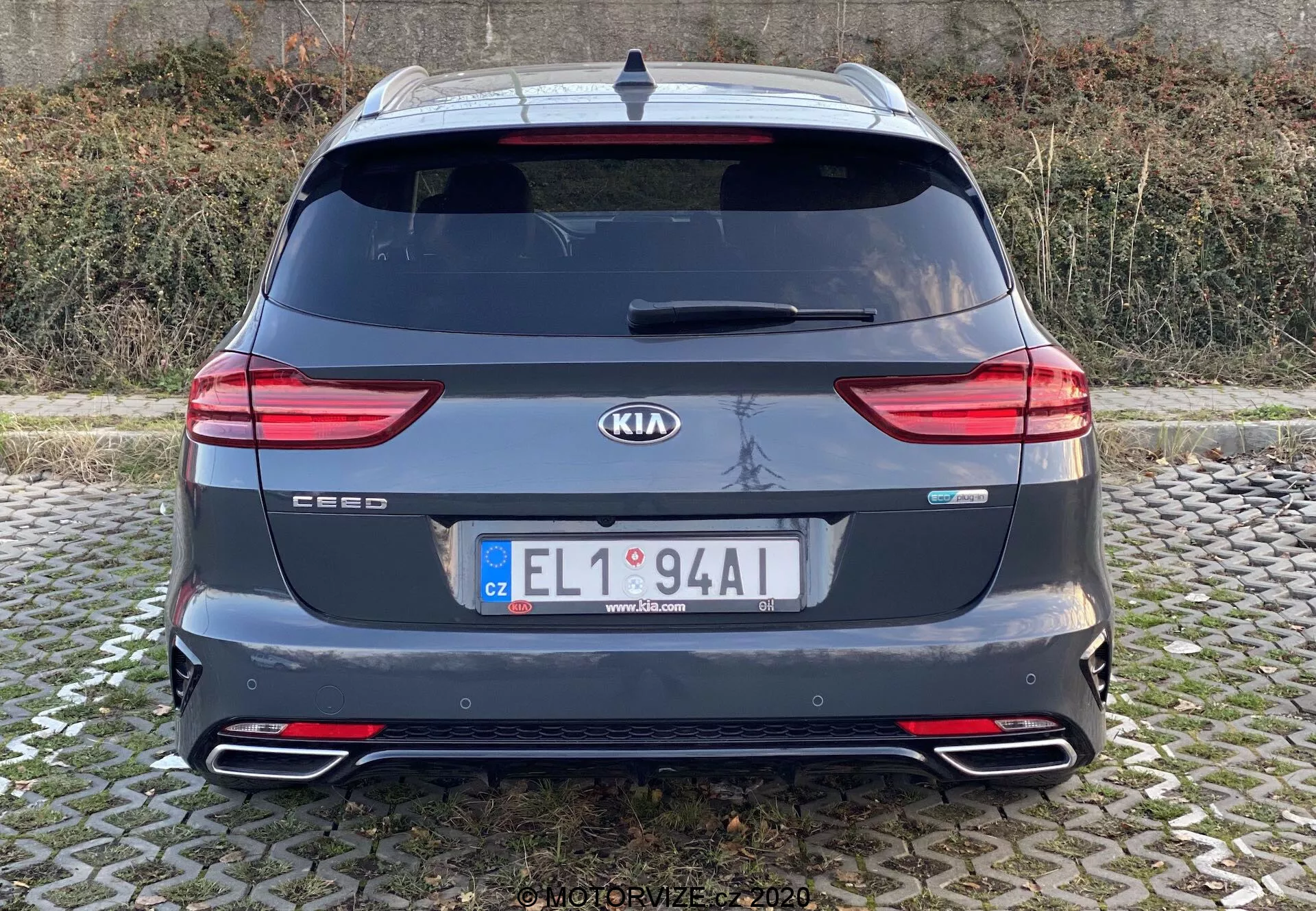 Egy 2018-as Kia Ceed hátsó nézete, amely megmutatja az autó teljes hátsó részét márka- és modellszalagokkal, modern LED-es hátsó lámpákkal, hátsó ablakkal, dupla kipufogóvégekkel, hátsó lökhárítóval reflektorokkal, tetőspoilert, antennát és hátsó parkolószenzorokat. A kép tiszta, szemmagasságban készült természetes megvilágítás mellett felhős körülmények között.
