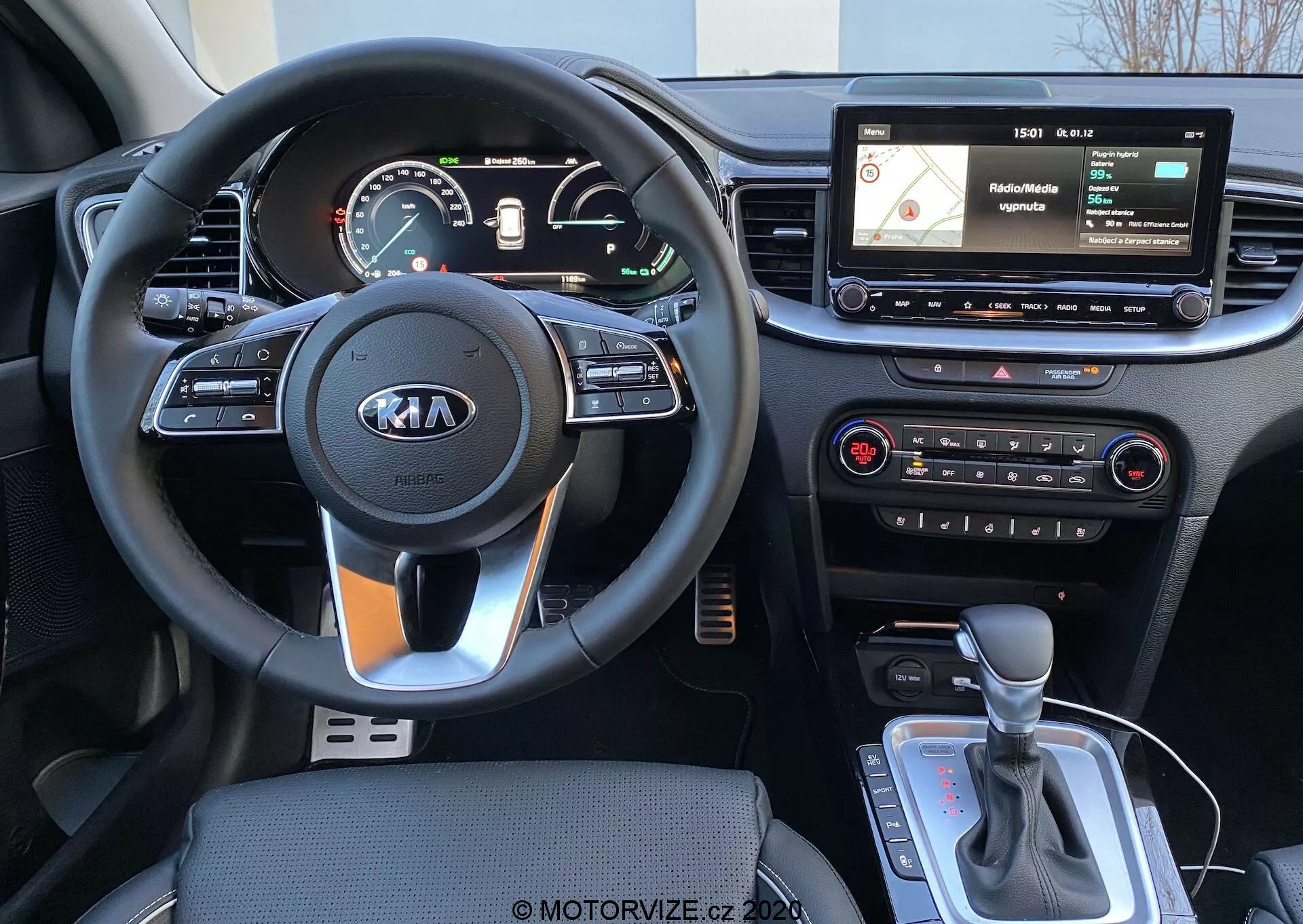 2018-as Kia Ceed belső nézete a vezetőülés perspektívájából, amelyen háromküllős kormánykerék látható Kia logóval, kormányra szerelt vezérlők, egy digitális/analóg műszercsoport, egy lebegő infotainment kijelző navigációval és média interfésszel, fizikai klímavezérlők, valamint egy automata váltó kar, lehetséges vezetési mód kiválasztóval vagy elektromos kézifékkel.