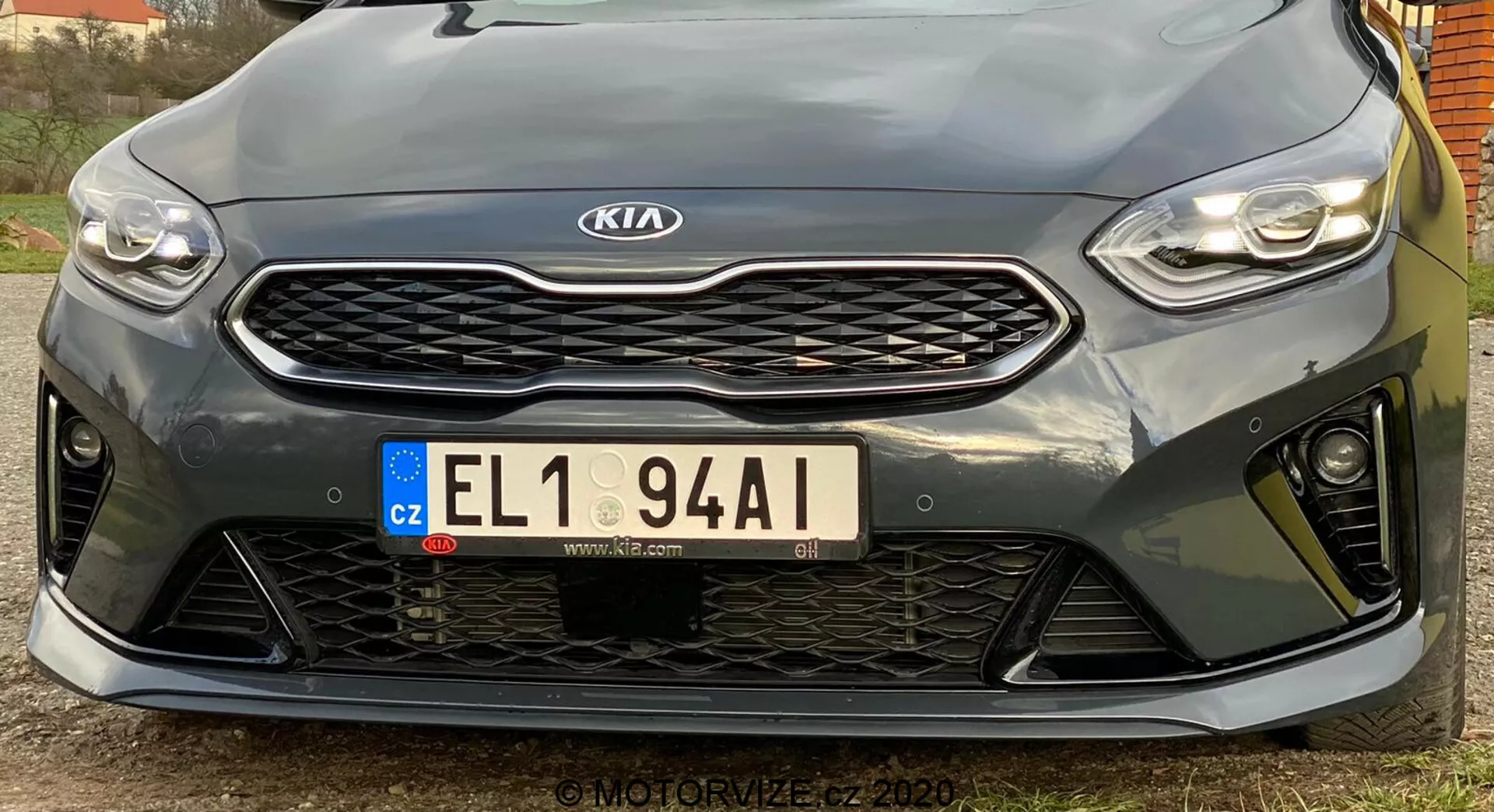 Ez a kép egy 2018-as Kia Ceed jármű elülső részét ábrázolja alacsony szögből. Kiemeli az elegáns, vízszintesen orientált LED-fényszórókat, a kiemelkedő méhsejt-mintás hűtőrácsot középen a Kia emblémával, az európai stílusú rendszámtáblát a Cseh Köztársaságból és a sportos első lökhárítót nagy nyílásokkal. A közeli nézet kiemeli a hűtőrács alatti parkolószenzorokat. A sportos dizájn nagyobb teljesítményű felszereltségi szintet sugall, bár a pontos specifikációk nem egyértelműek. A nagy felbontású kép rögzíti a tervezési részleteket és kontúrokat, enyhén balra eltolt szöggel.