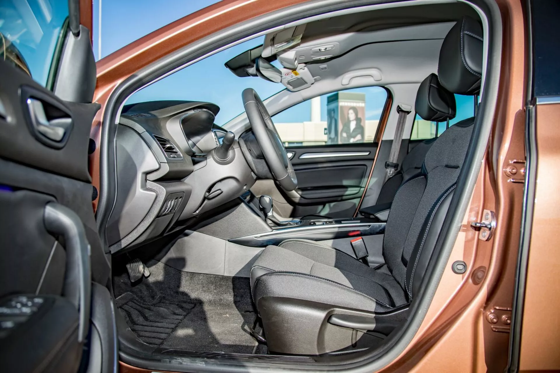 2009-es Kia Ceed Pro-Cee'd belső nézete az nyitott vezetőoldali ajtón keresztül, bemutatva a sötét szövetből készült első üléseket, a kormányra integrált vezérlőket, részben látható műszerfalat az infotainment képernyővel, középkonzolt váltókarral, autószőnyegeket és kéttonusú színsémát