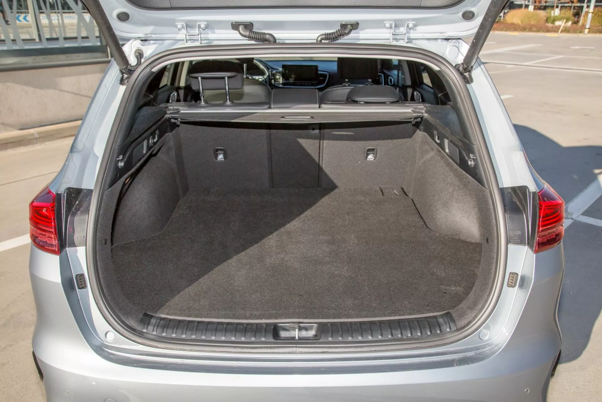 Egy 2009-es Kia Cee'd ferdehátú autó hátsó csomagtartójának belső tere, nyitott csomagtérajtóval, bemutatva a tágas tiszta rakodóteret, szőnyegpadlót, visszahúzható fedőt és a potenciális belső világítást