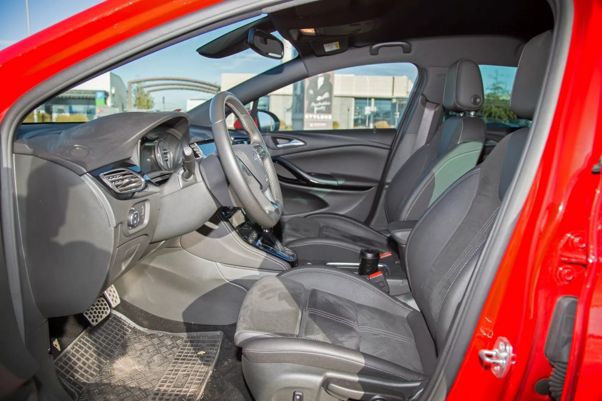 2009-es Kia cee'd belső terét bemutató kép, amely tartalmaz a bal oldalon elhelyezett kormányt vezérlőgombokkal, központi infotainment képernyőt, látható műszerfalat, további vezérlőgombokkal ellátott középkonzolt, fejtámlás, részben bőrhatású kárpitozású üléseket, részletezett ajtó belsőt vezérlőgombokkal, kéttónusú színsémát, a visszapillantó és a vezető oldali tükröt, strapabíró szőnyegeket és légzsák jelzőfényeket, átfogó design és technológia-orientált jellemzők bemutatása külső oldalnézetből