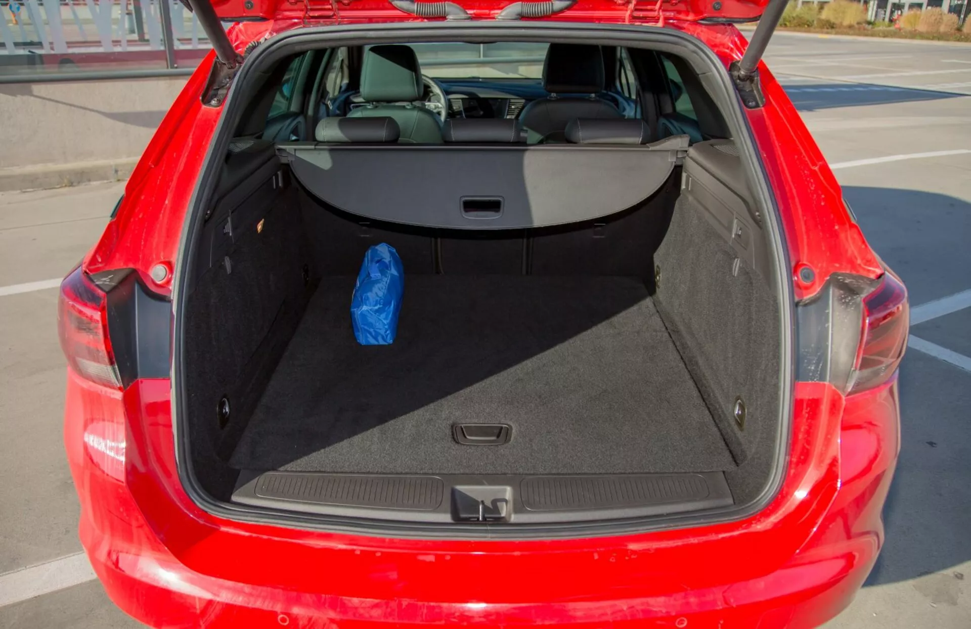 Részletes nézet a piros 2009-es Kia Cee'd nyitott csomagtartójáról, amely tágas tárolóteret és 60/40 arányban osztható hátsó üléseket mutat be, egyetlen kék zacskóval szemléltetve a használhatóságot.