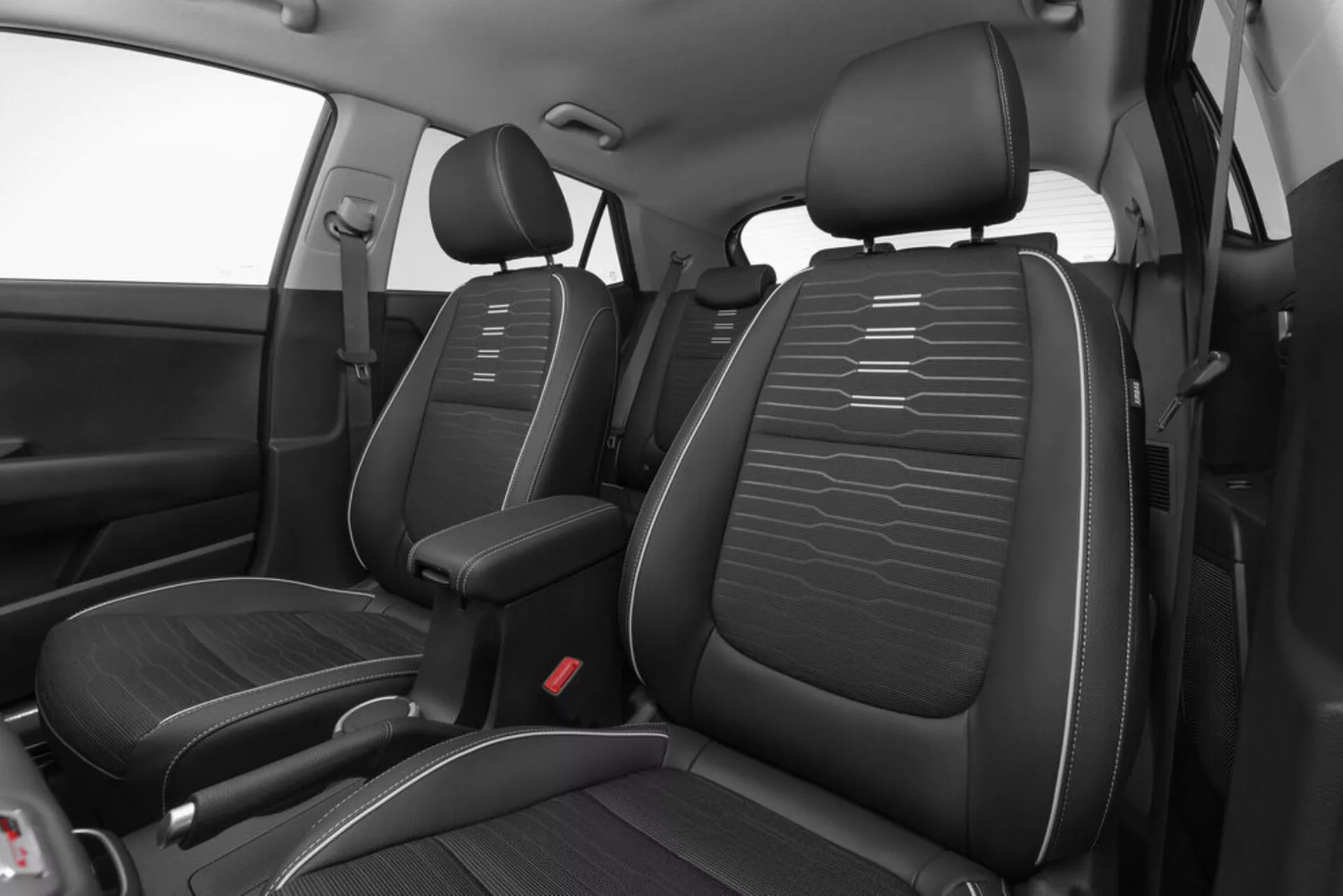 Magas szögből készült kép a Kia Stonic 2017-es modelljének első belső teréről, bemutatva a fekete műbőr üléseket vízszintes varrással, a középkonzolt és a piros biztonsági övzáródási pontokat a tervezésre és elrendezésre összpontosítva