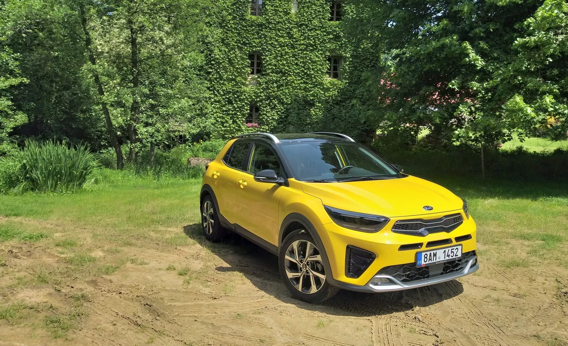 Vibráló sárga Kia Stonic 2017 crossover SUV háromnegyedes első nézetben, kiemelve az első hűtőrácsot, LED fényszórókat, motorháztetőt és a vezető oldalát, természetes háttérrel szemben, napsütéses tisztáson, megmutatva a könnyű terepjáró képességeit, sportos ötvözött kerekeket és modern design elemeket.