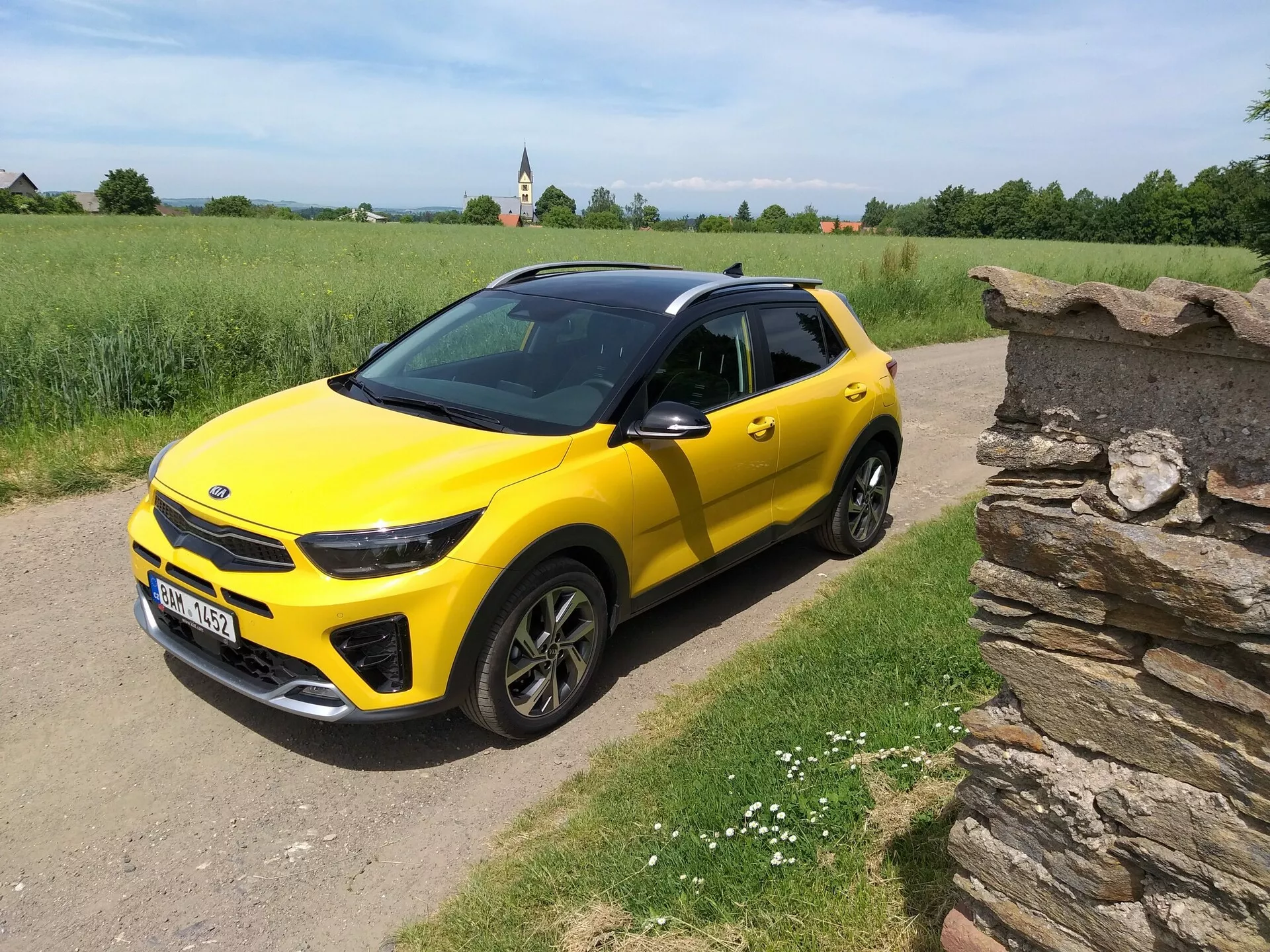 Világossárga Kia Stonic 2017 kompakt SUV fekete tetővel, amely elölről háromnegyedes szögben mutatja elegáns tervezését és dinamikus kontúrjait egy vidéki murvás úton