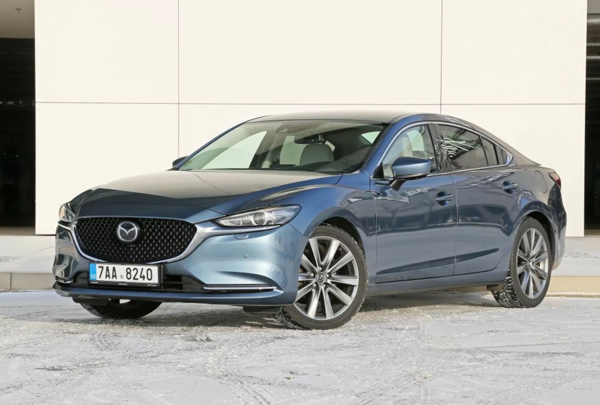 2013-as kék Mazda 6 szedán, amely háromnegyedes elölnézetben mutatja be a rácsot, az emblémát, a stílusos fényszórókat és az ötvözött kerekeket téli aszfalton