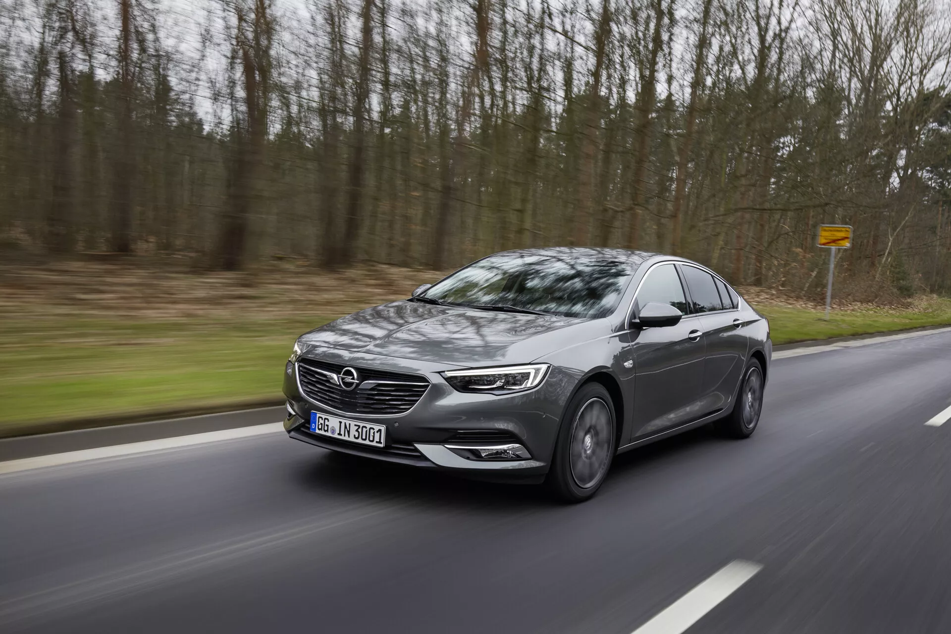 2013-as Opel Insignia modern szedán mozgásban egy kanyargós úton az erdőn keresztül, oldalprofilját bemutatva LED fényszórókkal, nagy hűtőráccsal, ötvözött kerekekkel, irányjelzőkkel ellátott oldalsó tükrökkel és sötétített ablakokkal