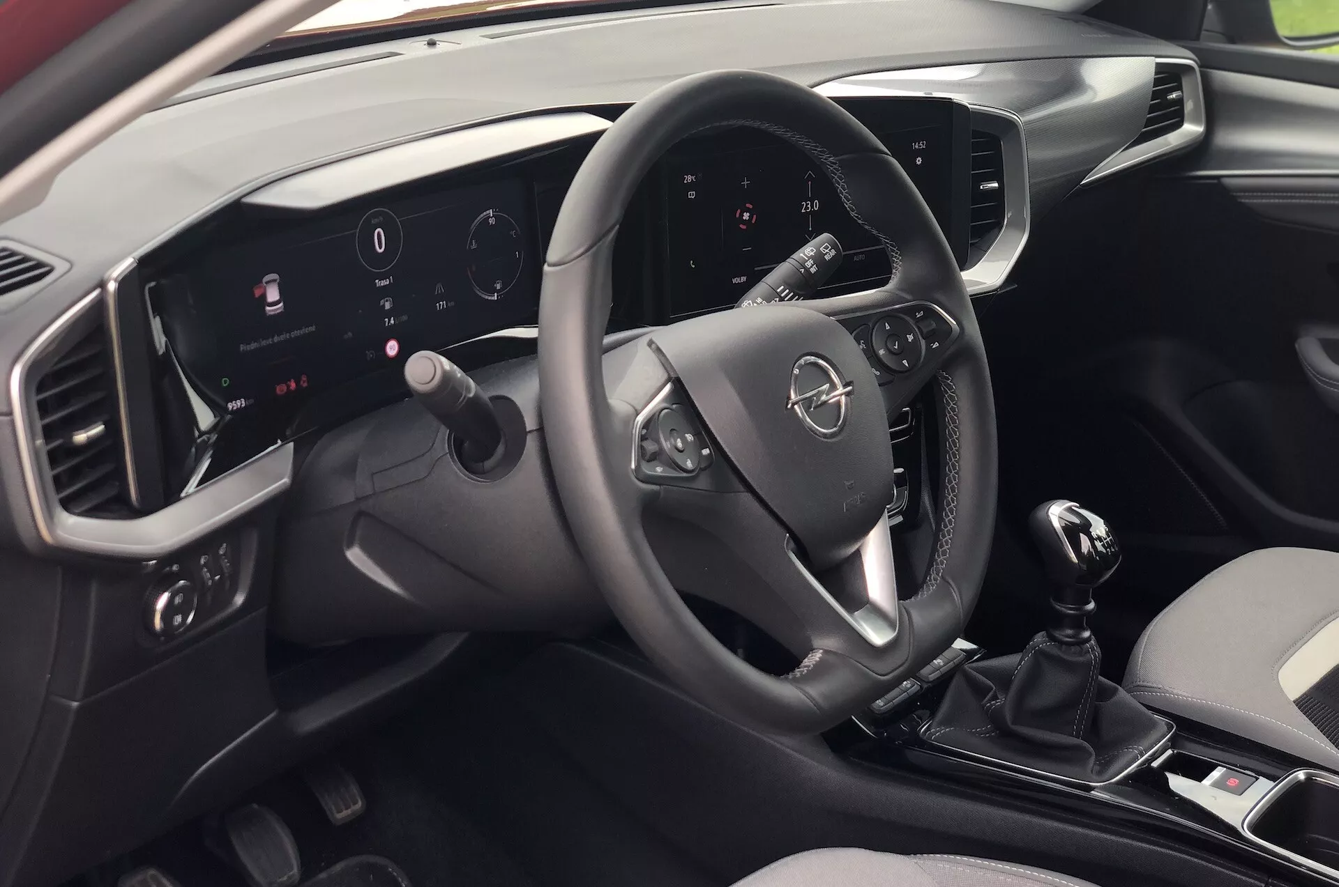 A 2021-es Opel Mokka belső nézete a jobb oldalon ülő hátsó utas perspektívájából, amely bemutatja a modern műszerfalat, a multifunkciós kormánykereket, a megvilágított digitális műszeregységet, az érintőképernyős információs és szórakoztató rendszert, a manuális sebességváltót és az elegáns kéttónusú formatervezést.