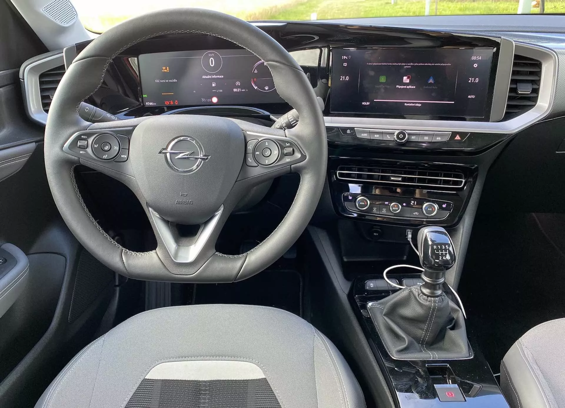 A 2021-es Opel Mokka belső tere az első utas perspektívájából, háromküllős kormánykerékkel, beépített vezérlőkkel, teljesen digitális műszerfallal, központi infotainment érintőképernyővel, klímaberendezéssel és navigációval, valamint manuális sebességváltóval. Az elrendezés kettős vezérlőrendszert és további gombokat tartalmaz a vezetési módokhoz, textil kárpitozással.