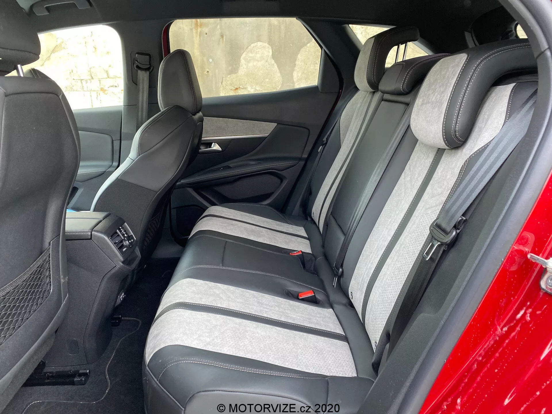 A 2021-es Peugeot 3008 belső terének felvétele, amely a hátsó ülésre összpontosít, kívülről, a vezető oldala felé szögelve nézve. A hátsó ülések kéttónusú anyagból készültek, sötét és világosszürke kombinációjával, valamint texturált csíkos mintával. A megfelelően összehangolt, felemelt fejtámlák láthatóak. A első sor ülőhelyei és a középső konzol része szintén látható. A hátsó ülések hárompontos biztonsági övekkel és pohártartókkal integrált karfával rendelkeznek. Az ajtó panelek az ülések színeihez illeszkednek, hangszórórácsokkal és energiavezérlő szekciókkal.