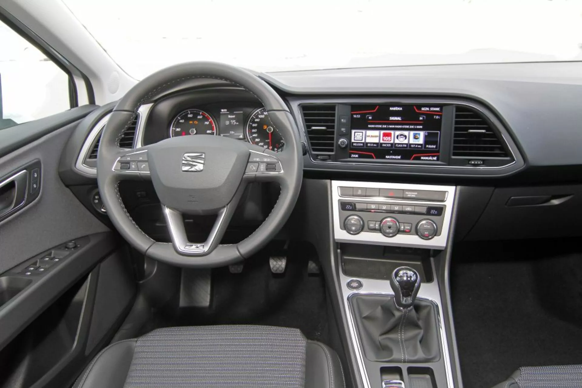 2013-as Peugeot 308 SW belső nézete, amelyen látható a logoval és multifunkciós vezérlőkkel ellátott kormánykerék, analóg sebességmérő és fordulatszámmérő digitális kijelzővel, érintőképernyős infotainment rendszer az műszerfalon, manuális klímavezérlő gombok a középkonzolon, manuális váltókar, és praktikus sötét szövet kárpitozás.