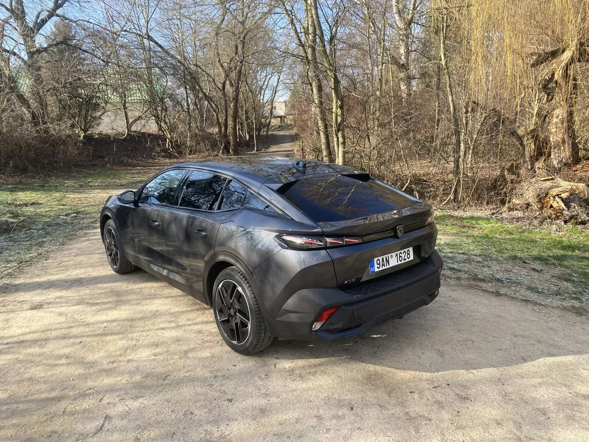 A Peugeot 408 2023 hátsó háromnegyedes nézete, amely bemutatja modern crossover kialakítását, kiemelve a csomagtérajtót, az elegáns hátsó ablakot és a karosszéria oldalába nyúló vízszintes hátsó lámpákat, rálátással az ötvözött kerékre, formált oldalprofilra és kéttonusú külsőre a természetes napfény alatt