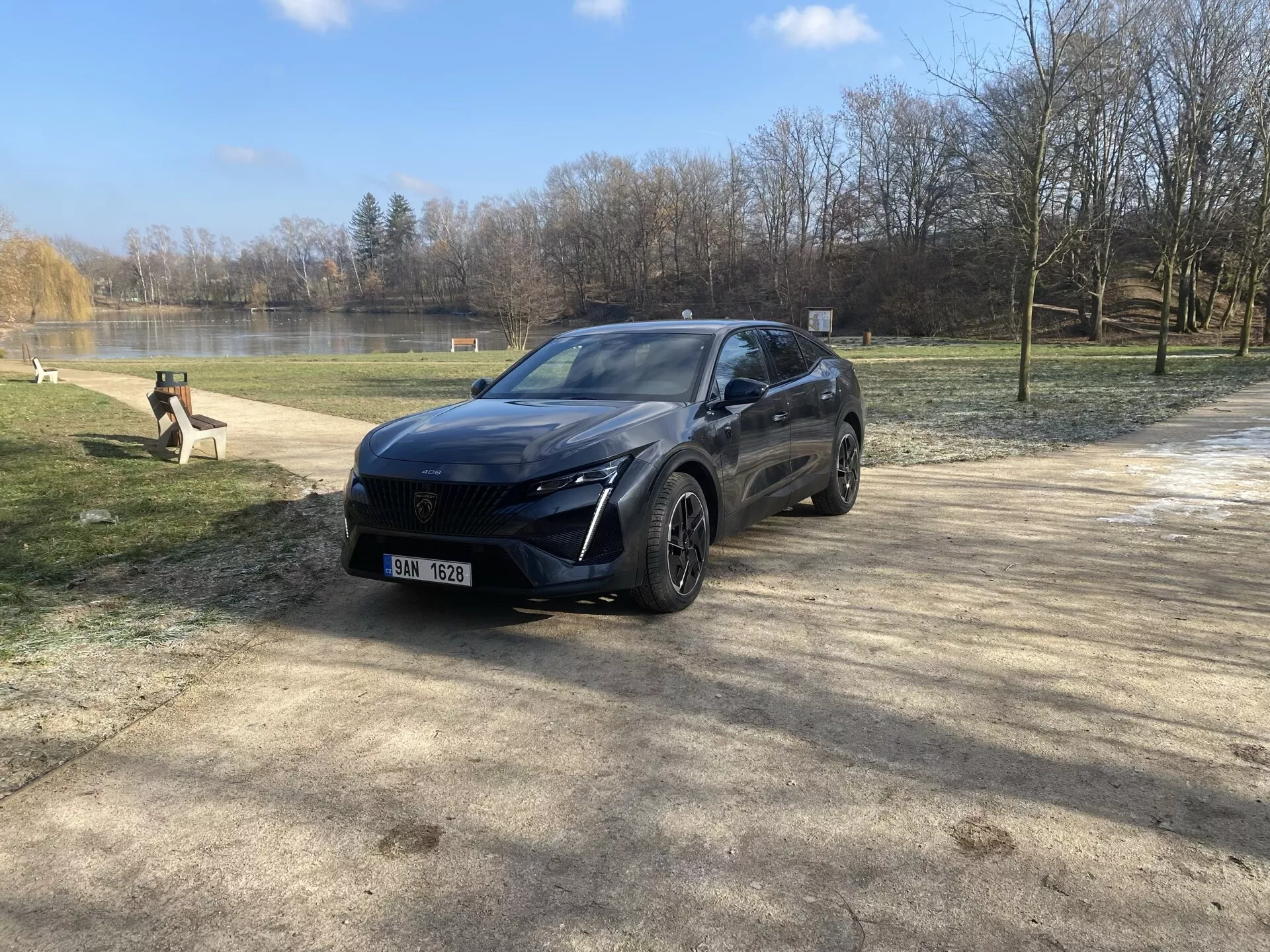 2023-as Peugeot 408 parkol természeti környezetben tél végén vagy kora tavasszal, bemutatva modern crossover dizájnját, LED fényszóróit, előlapi szenzor rendszerét, ötvözött kerekeit és prémium befejezését egy első háromnegyedes szögből nézve a napfényben lencsefény visszaverődéssel.