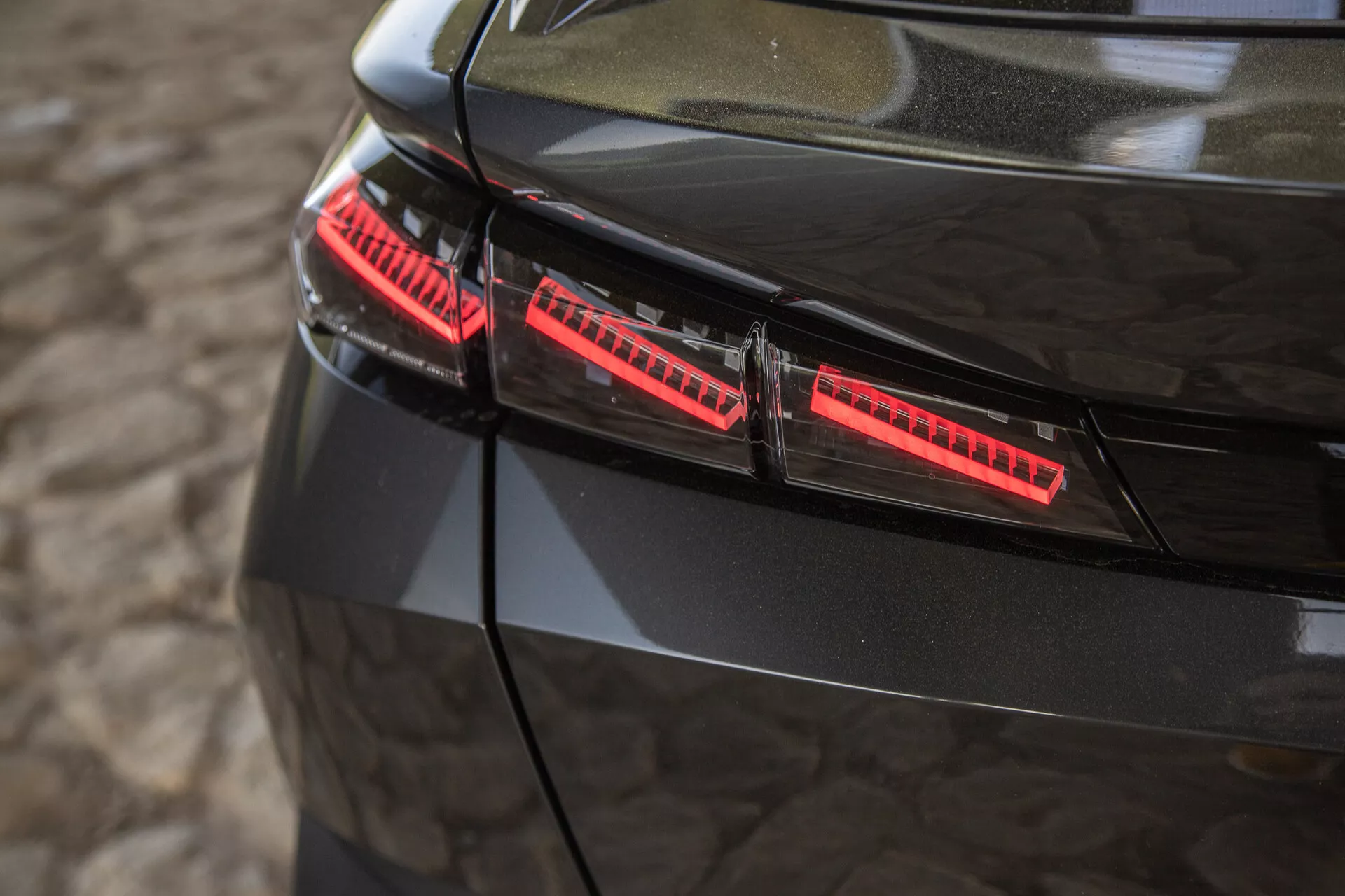 Közeli nézet a 2023-as Peugeot 408 fényes fekete hátsó lámpáira, amelyek modern LED elemeket és elegáns design akcentusokat mutatnak, kissé emelt szögből fotózva
