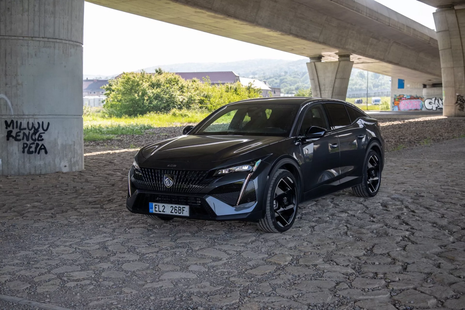 2023-as Peugeot 408 háromnegyed szögből fényképezve, kiemelve az elegáns LED fényszórókat, mintás hűtőrácsot és sportos aerodinamikai első lökhárítót természetes nappali fényben egy burkolt területen, egy felüljáró alatt