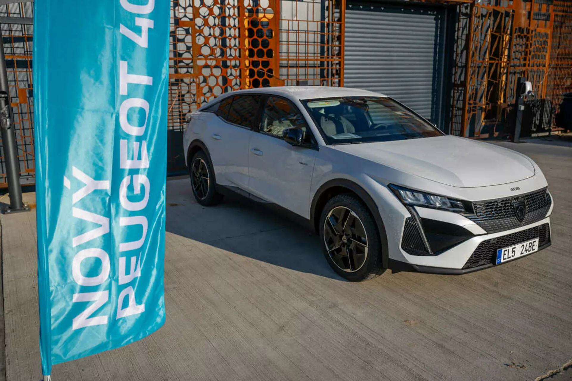 2023-as fehér Peugeot 408 parkol a szabadban ipari építészet háttérrel, bemutatva a jármű tervezési és technológiai jellemzőit a természetes nappali fényben