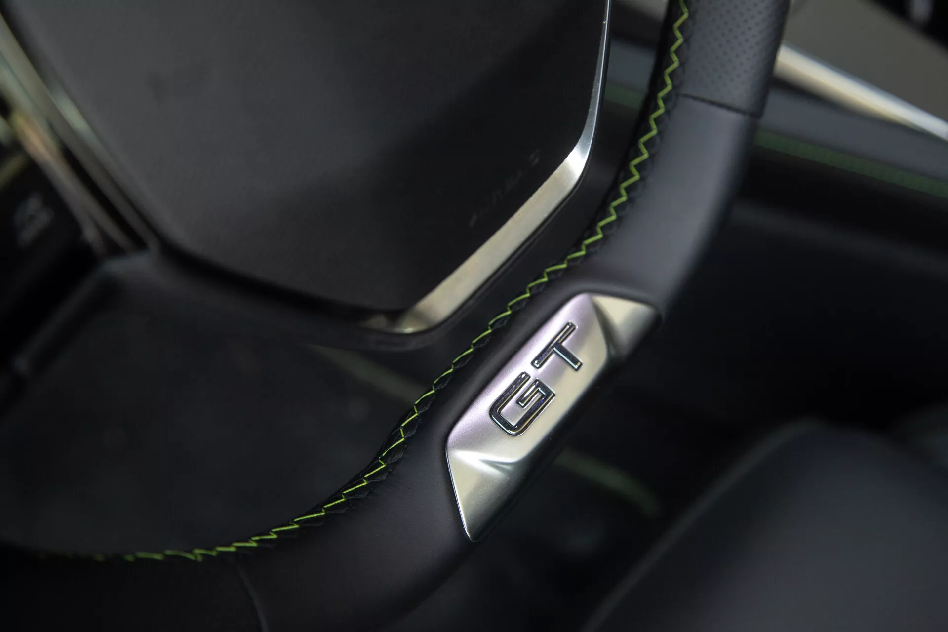 Közeli kép a Peugeot 408 2023 autó kormányrészéről és műszerfalról, fekete bőr kormánykerék zöld varrással és GT jelzéssel, luxust és sportosságot hangsúlyozva