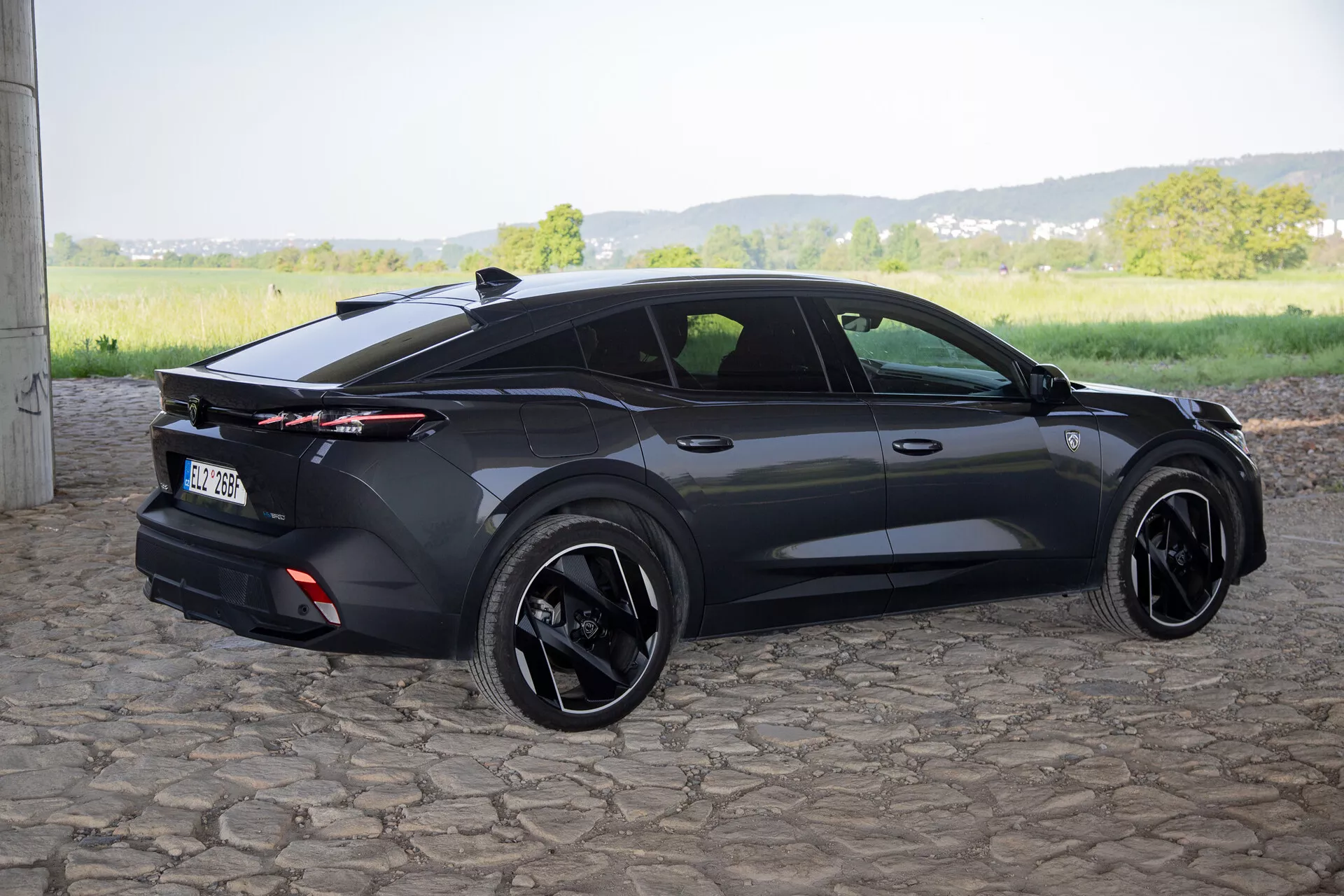 2023-as Peugeot 408, háromnegyedes hátsó szögből fotózva, kiemelve a sportos ferdehátú kialakítását, beépített hátsó légterelőjét teljes hosszban elhelyezkedő hátsó lámpákkal, fekete ötvözött keréktárcsákkal és korszerű funkciókkal, mint az ajtókilincsek és az oldalsó tükrök intégrált irányjelzőivel, természetes nappali fényben