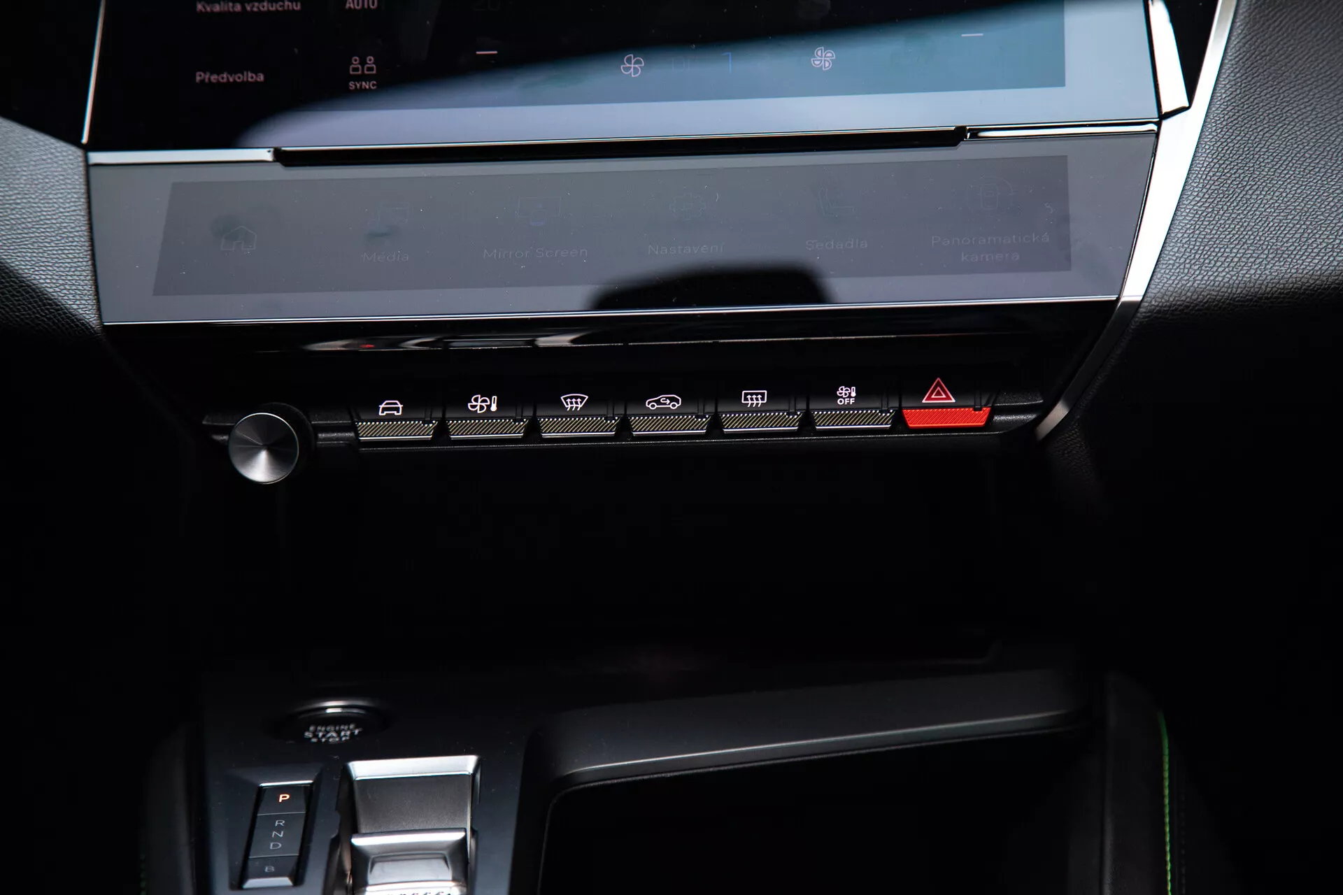 2023-as Peugeot 408 központi műszerfala az infotainment rendszer kikapcsolt érintőképernyőjével, az érintésérzékelős gombokkal ellátott klímavezérlő panellel és az elektronikus váltóterület részével, puha környezeti fényekkel megvilágítva, amelyek kiemelik a modern, elegáns tervezést sötét tónusokkal és fémes akcentusokkal.