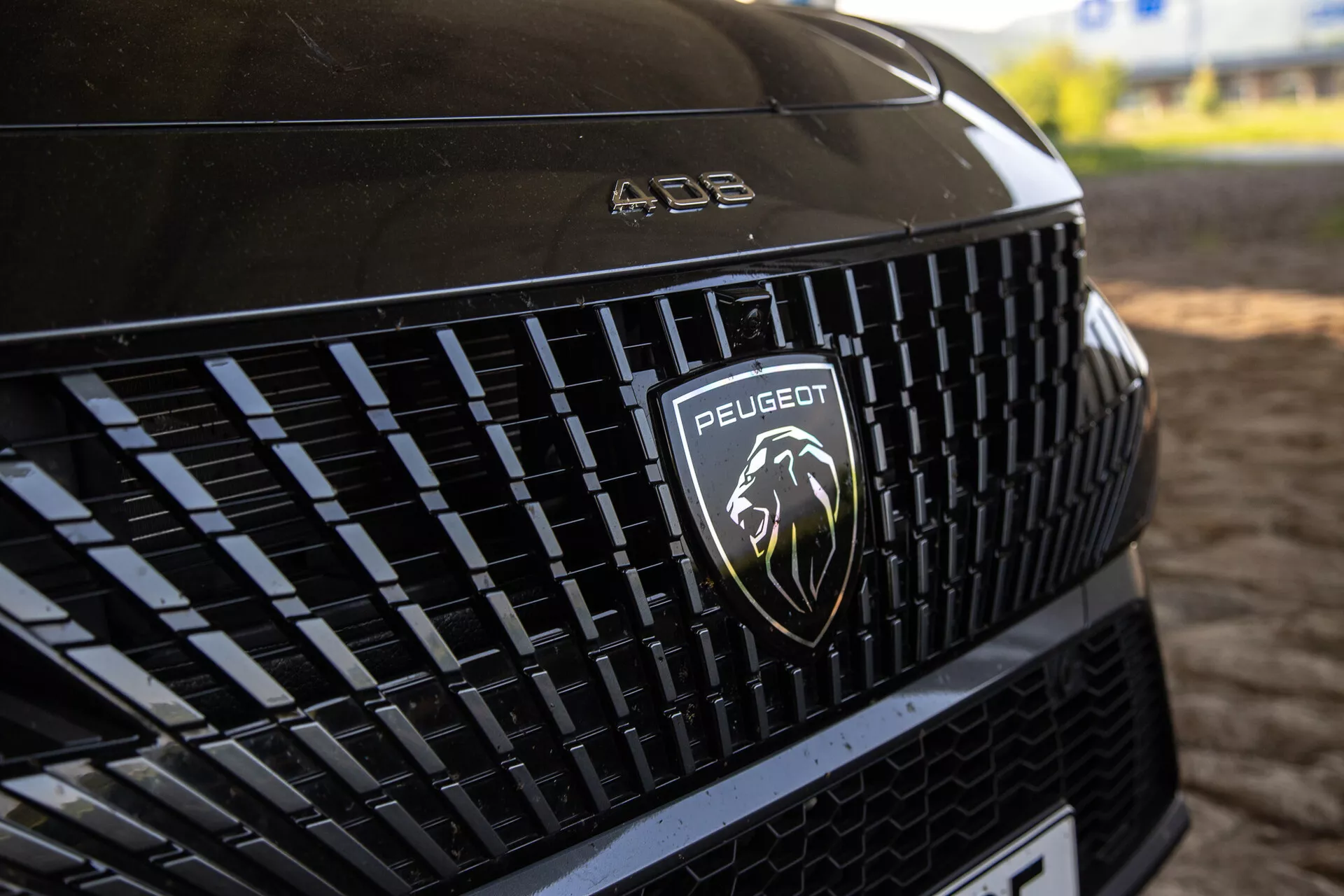 Részletes nézet a Peugeot 408 2023 első hűtőrácsáról, amely az összetett mintát és az ezüst színű oroszlán logót mutatja természetes fényben