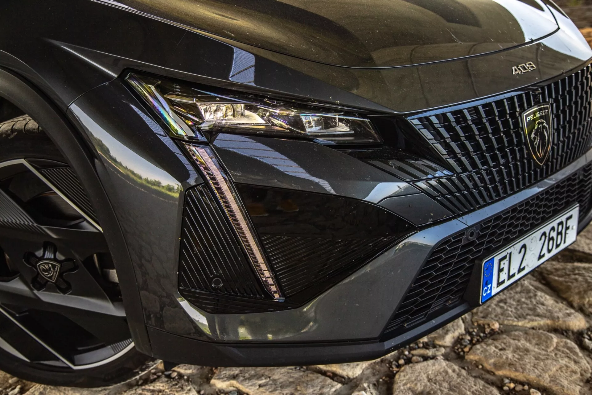 Közeli nézet a 2023-as Peugeot 408 első bal sarkára, amely részletesen mutatja a fényszóróegységet, a rács szakaszt, a motorháztetőt és a kereket modern LED technológiával és luxus design elemekkel.