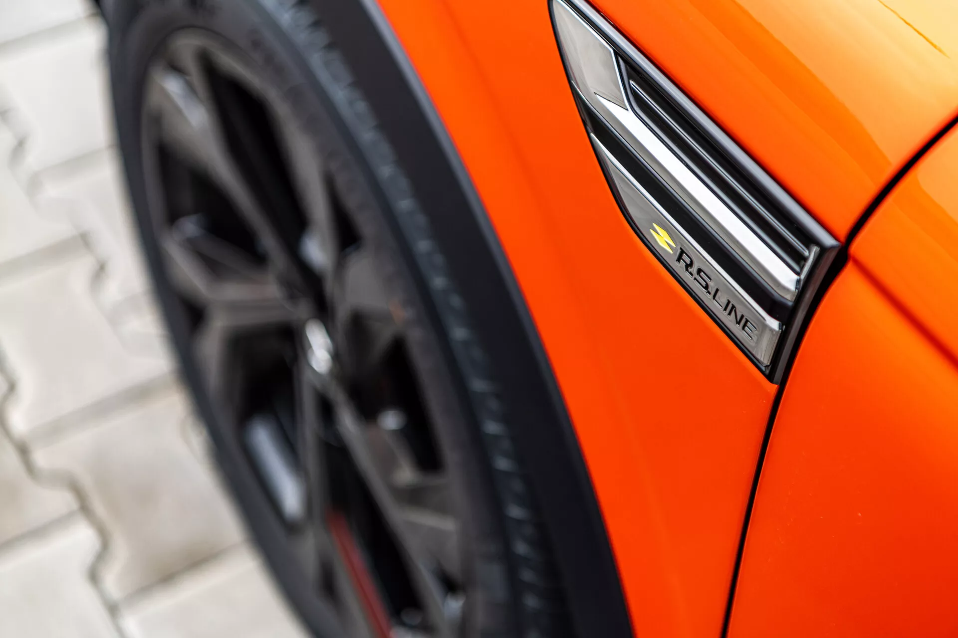 Közeli nézet egy narancssárga 2021-es Renault Arkanáról, amely az oldalprofilra összpontosít az S-Line jelvény, a sárvédő és a sportos keréktervezés megjelenítésével alacsony szögben