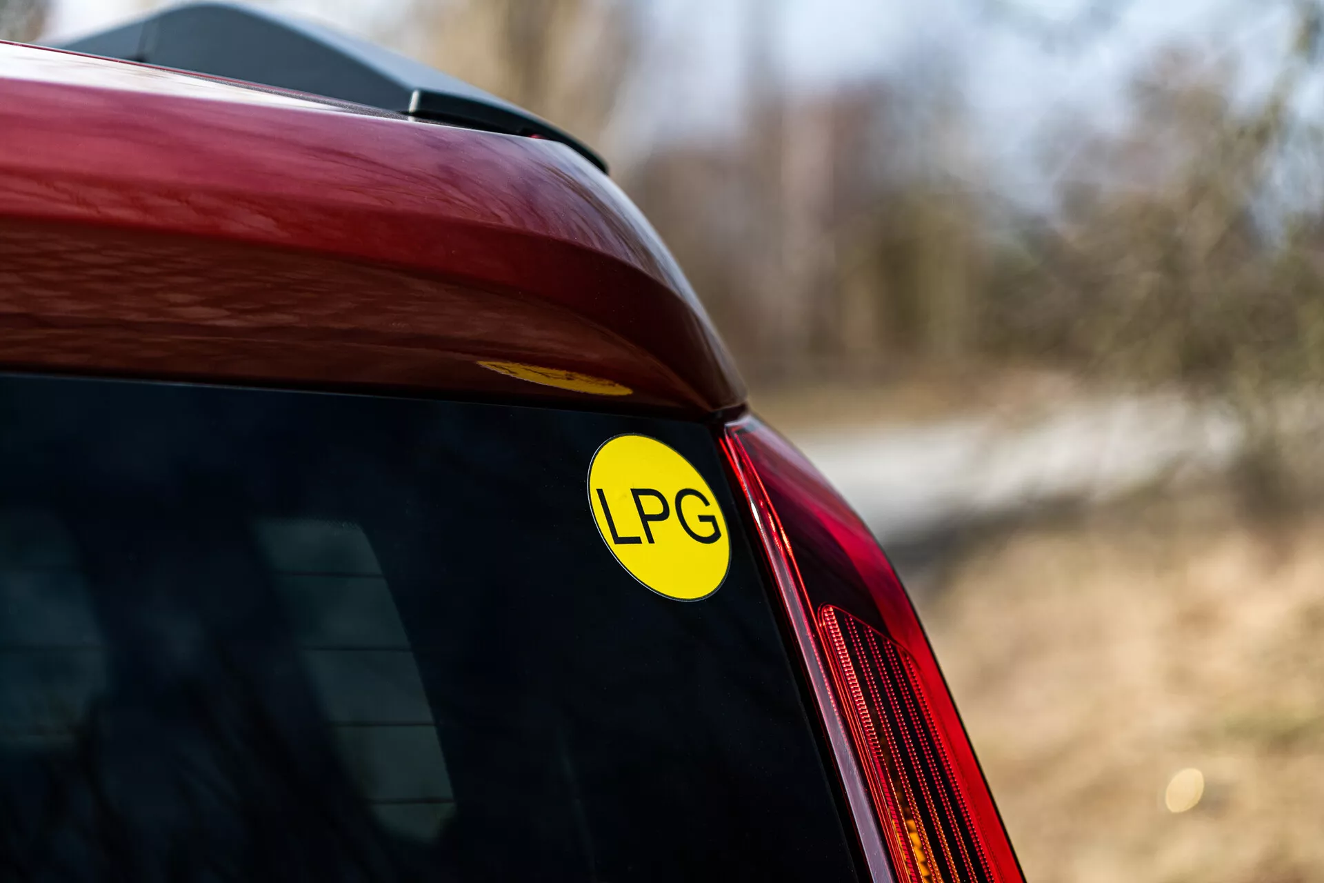 Közeli kép a 2021-es piros Renault Arkana hátsó sarkáról, amely az LPG matricát mutatja a cseppfolyósított kőolajgáz használati képességére, a hátsó szélvédő és oldalpanel találkozására összpontosítva, természetes külső fényben