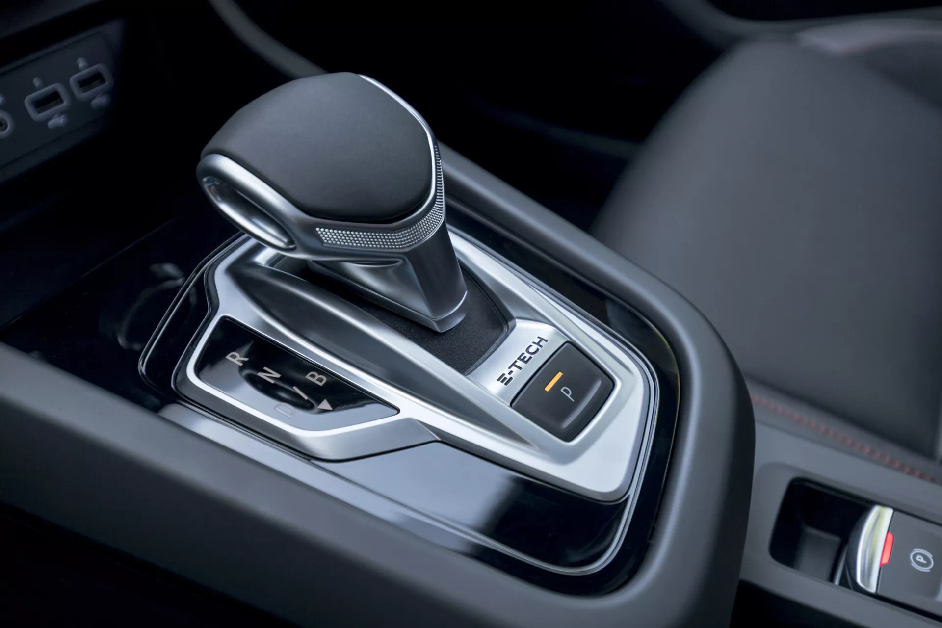 Közeli nézet a 2021-es Renault Arkana automata váltókarjáról a jármű belsejében, modern tervezésű, bőrrel bevont gombbal, króm díszítésekkel és elektronikus parkolófék vezérléssel.