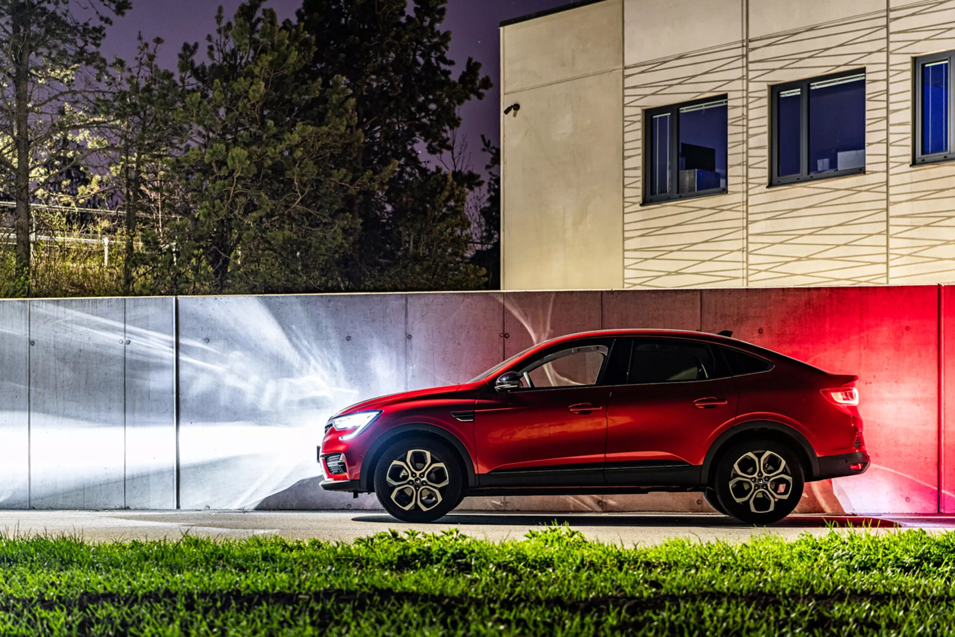 2021-es Renault Arkana oldalnézete éjszaka, kiemelve az elegáns piros színét, sportos tervezését és fejlett funkcióit stílusos városi háttérrel szemben