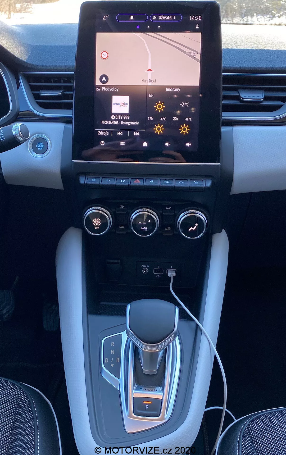 A Renault Captur 2020 belseje, amely a középkonzolt és a műszerfalat mutatja nagy érintőképernyős infotainment rendszerrel, amely a navigációs térképet jeleníti meg, dupla zónás klímaberendezési vezérlőkkel, elektronikus váltógombokkal, pohártartókkal, kefélt fém akcentusokkal és esetleges luxuskivitelű felületekkel.