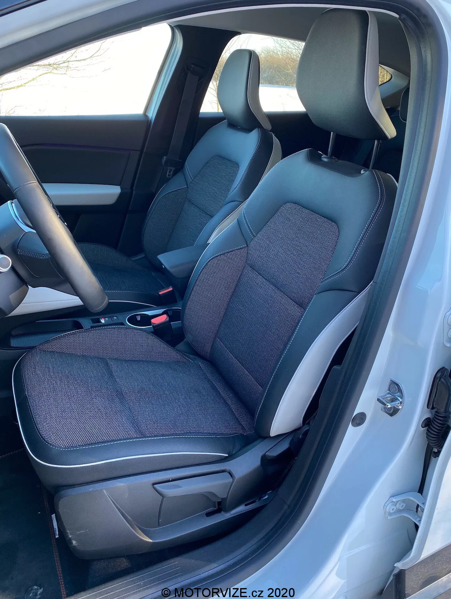 A Renault Captur 2020 belső nézete a bal oldalról, a vezető ajtajának nyitott állapotával, fekete és szürke szövet és bőr ülésekkel, középkonzollal, kormánykerékkel és a műszerfal részével.