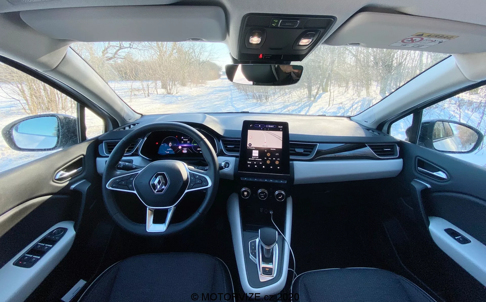 Egy Renault Captur 2020 belső nézete a hátsó ülésről előre nézve, bemutatva a sötét színű kárpitozást, a középső visszapillantó tükröt, a multifunkciós kormány mögötti megvilágított digitális műszerfalat, a középkonzol érintőkijelzős információs és szórakoztató rendszerét, valamint az elektromos ablakok, az oldalsó tükrök, a klímavezérlés és valószínűleg a napfénytető és a vészhelyzeti SOS gombok kezelőszerveit.