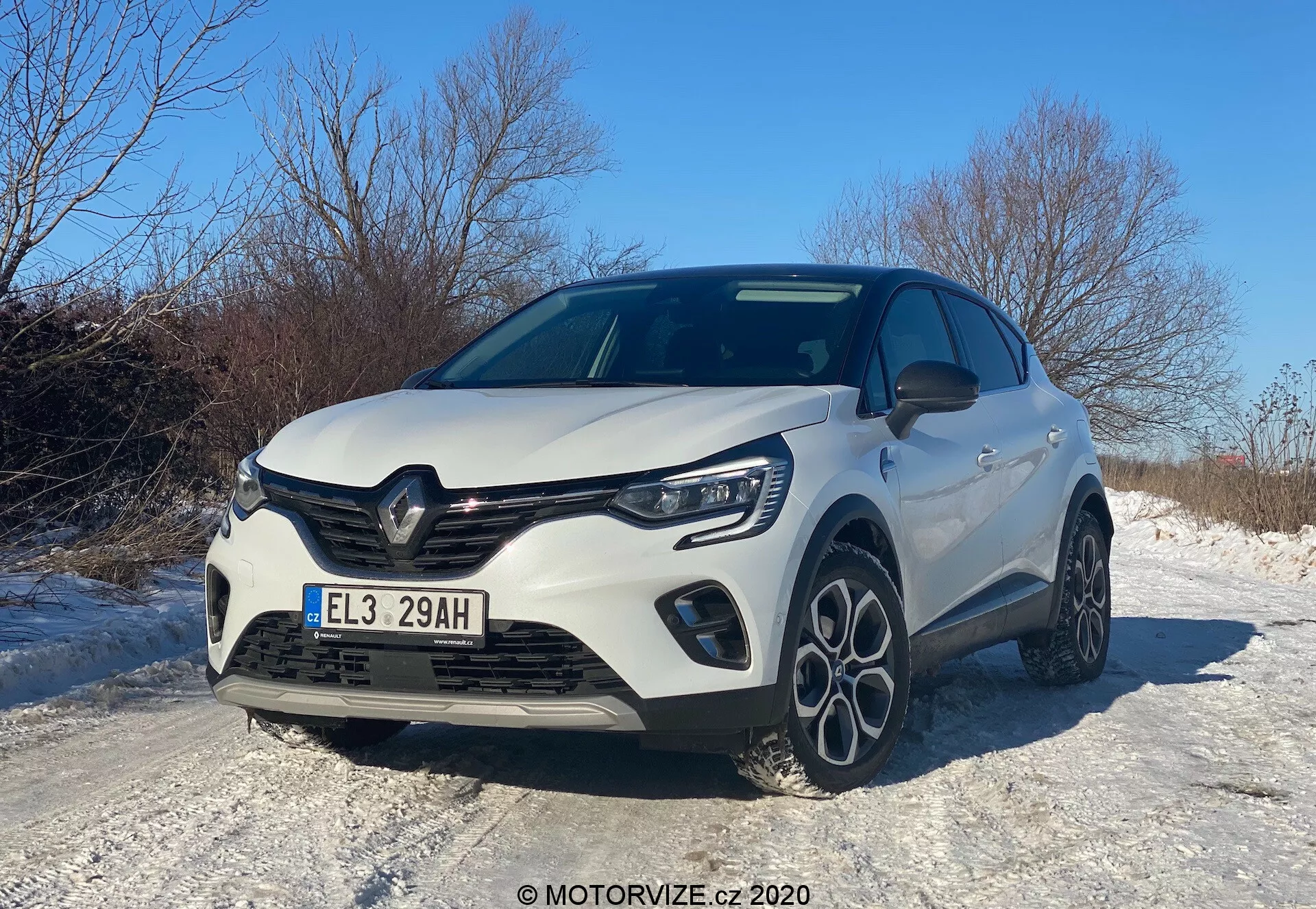 Modern hatchback jármű Renault Captur 2020, amelyet alacsony, első háromnegyedes szögből kaptak el, bemutatva az autó első hűtőrácsát, motorháztetőjét, LED-es fényszóróit, első lökhárítóját integrált ködlámpákkal és részleges oldalsó profilját. A dizájn elemei közé tartozik a gyártó emblémájával ellátott kiemelkedő hűtőrács, a formázott motorháztető vonalak és a többküllős könnyűfém kerekek, mindezt tiszta nappali ég alatt, sportos és aerodinamikus esztétikát tükrözve, amely valószínűleg egy továbbfejlesztett felszereltségi szintet vagy sportcsomagot emel ki. Az autó egy havas úton látható, ami arra utal, hogy a téli vezetéshez alkalmas tulajdonságokkal rendelkezik.