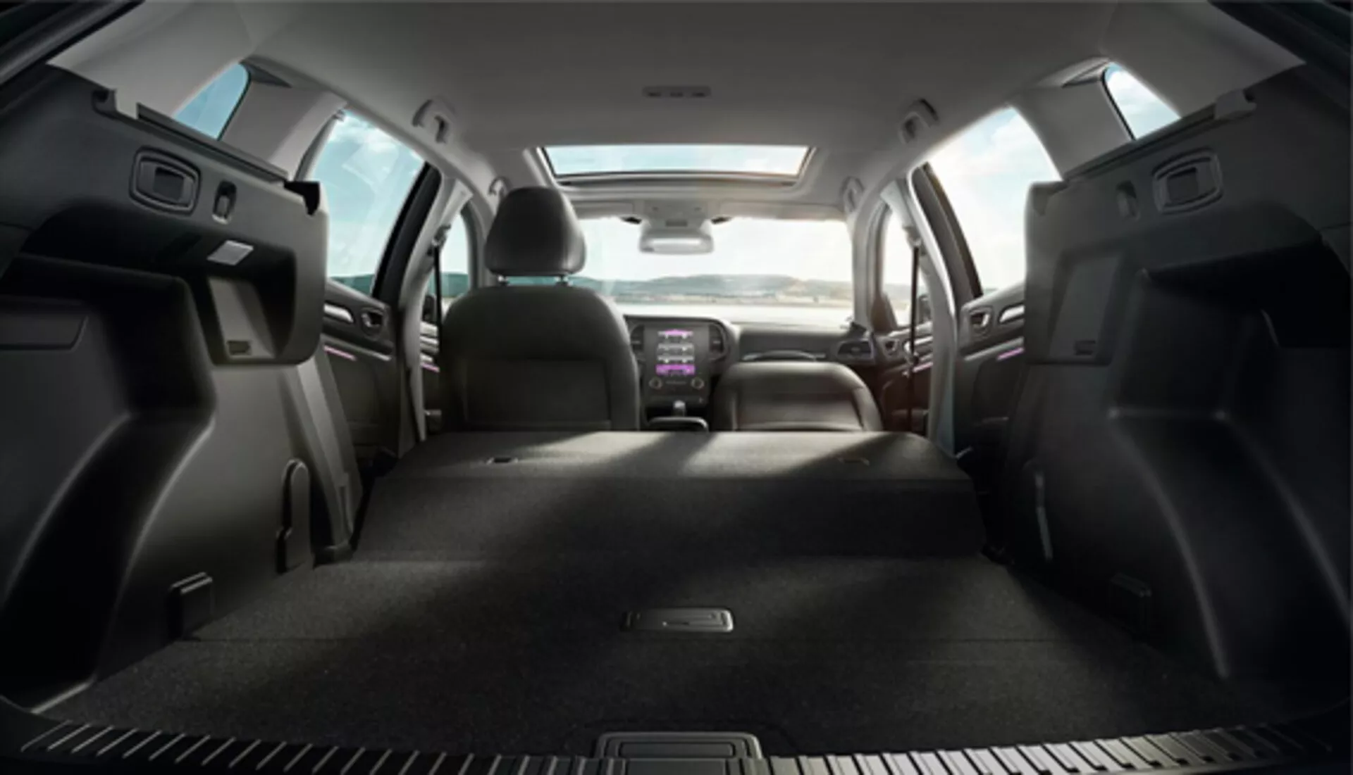 Renault Megane 2016 Grandtour belső nézet a csomagtartó területéről az előre felé, bemutatva az összehajtható hátsó üléseket, szövetből kárpitozott első üléseket fejtámlákkal, tárolózsebeket a hátsó ajtókon, pohártartókkal ellátott középkonzolt, megvilágított infotainment rendszert, és a klímavezérlés és a kormánykerék részleges nézetét, ami tágas és technológiával felszerelt kabinra utal.