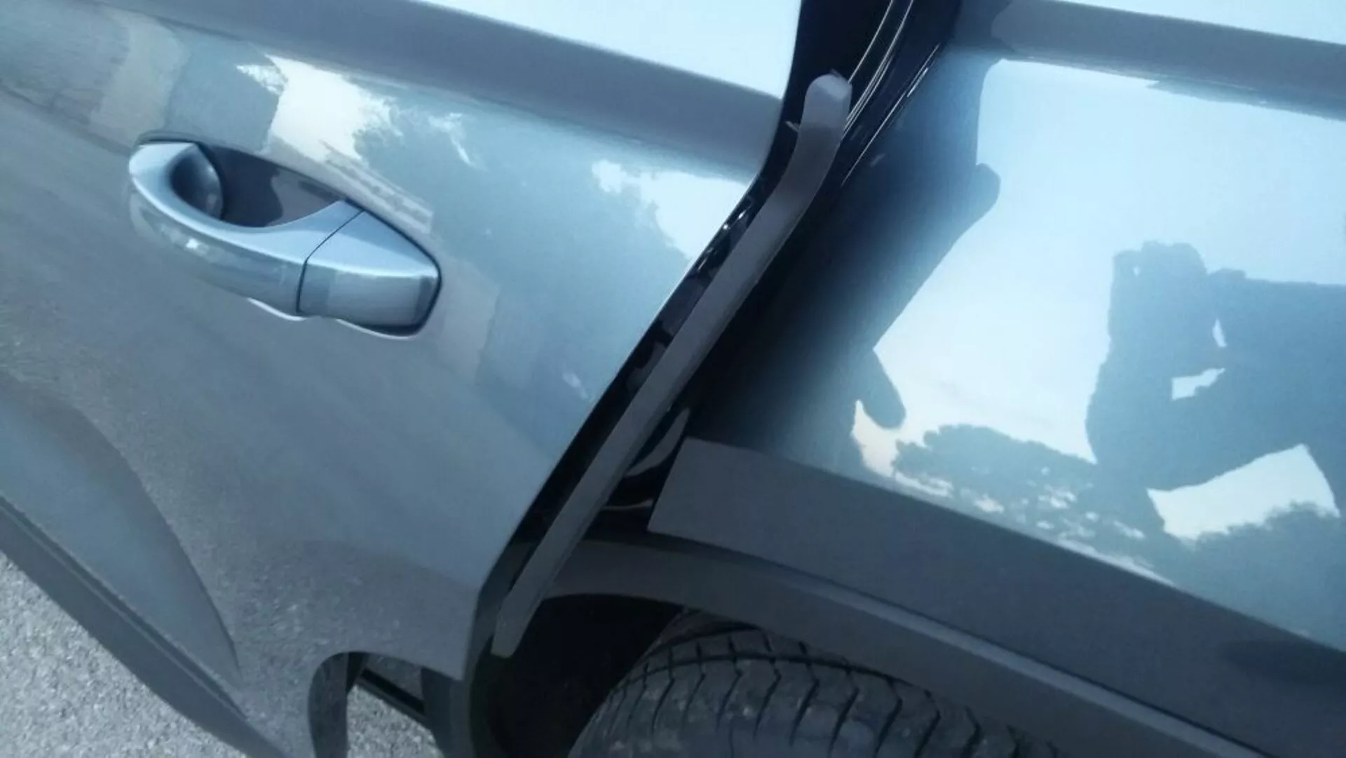 Részletes oldalnézetű kép a 2017-es Skoda Kodiaq-ról, amely az első utasajtó területére összpontosít, részleteket kiemelve az autó sötétszürke, tükröződő festékéről, a modern ajtókilincs tervezéséről és az integrált oldalsó küszöbről, diffúz külső megvilágítás mellett.