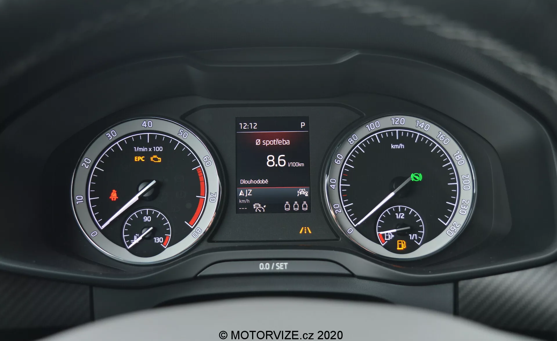 A Skoda Kodiaq 2017 műszerfalának közelképe a vezető szemszögéből, amely analóg és digitális műszerek keverékét mutatja a kormány mögött. A műszerfal tartalmaz egy fordulatszámmérőt narancssárga figyelmeztető lámpával, egy központi kijelzőt, amely különféle járműinformációkat jelenít meg, például az időt, a rögzítőfék állapotát, a sport módot, a hatótávolságot és a hőmérsékletet, valamint egy sebességmérőt üzemanyag-mutatóval és automatikus indítás/leállítás jelzővel.